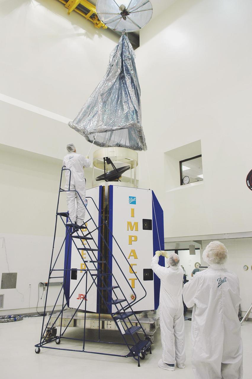 KENNEDY SPACE CENTER, FLA. -  At Astrotech Space Operations in Titusville, Fla., workers help guide an overhead crane holding a protective cover that will be placed over the Deep Impact spacecraft below. Deep Impact is being prepared for a move to the Hazardous Fuel Building and eventually shipment to Launch Pad 17-B, Cape Canaveral Air Force Station. Launch of Deep Impact is scheduled no earlier than Jan. 12.  A NASA Discovery mission, Deep Impact will probe beneath the surface of Comet Tempel 1 on July 4, 2005, when the comet is 83 million miles from Earth, and reveal the secrets of its interior.   After releasing a 3- by 3-foot projectile to crash onto the surface, Deep Impact’s flyby spacecraft will collect pictures and data of how the  crater forms, measuring the crater’s depth and diameter, as well as the composition of the interior of the crater and any material thrown out, and determining the changes in natural outgassing produced by the impact.  It will send the data back to Earth through the antennas of the Deep Space Network.