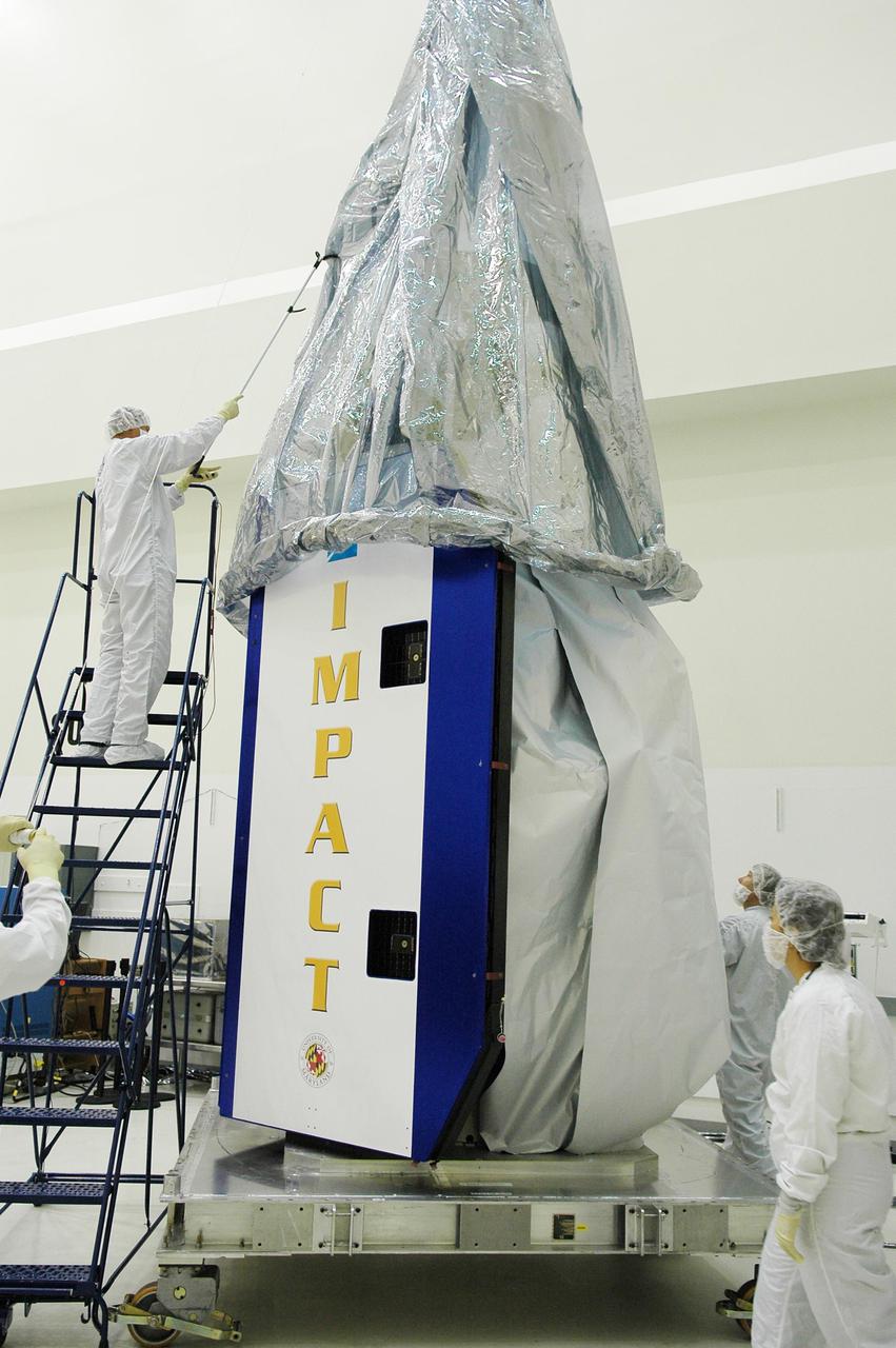 KENNEDY SPACE CENTER, FLA. -  At Astrotech Space Operations in Titusville, Fla., workers help guide the protective cover into place over the Deep Impact spacecraft below. Deep Impact is being prepared for a move to the Hazardous Fuel Building and eventually shipment to Launch Pad 17-B, Cape Canaveral Air Force Station.   Launch of Deep Impact is scheduled no earlier than Jan. 12.  A NASA Discovery mission, Deep Impact will probe beneath the surface of Comet Tempel 1 on July 4, 2005, when the comet is 83 million miles from Earth, and reveal the secrets of its interior.   After releasing a 3- by 3-foot projectile to crash onto the surface, Deep Impact’s flyby spacecraft will collect pictures and data of how the  crater forms, measuring the crater’s depth and diameter, as well as the composition of the interior of the crater and any material thrown out, and determining the changes in natural outgassing produced by the impact.  It will send the data back to Earth through the antennas of the Deep Space Network.
