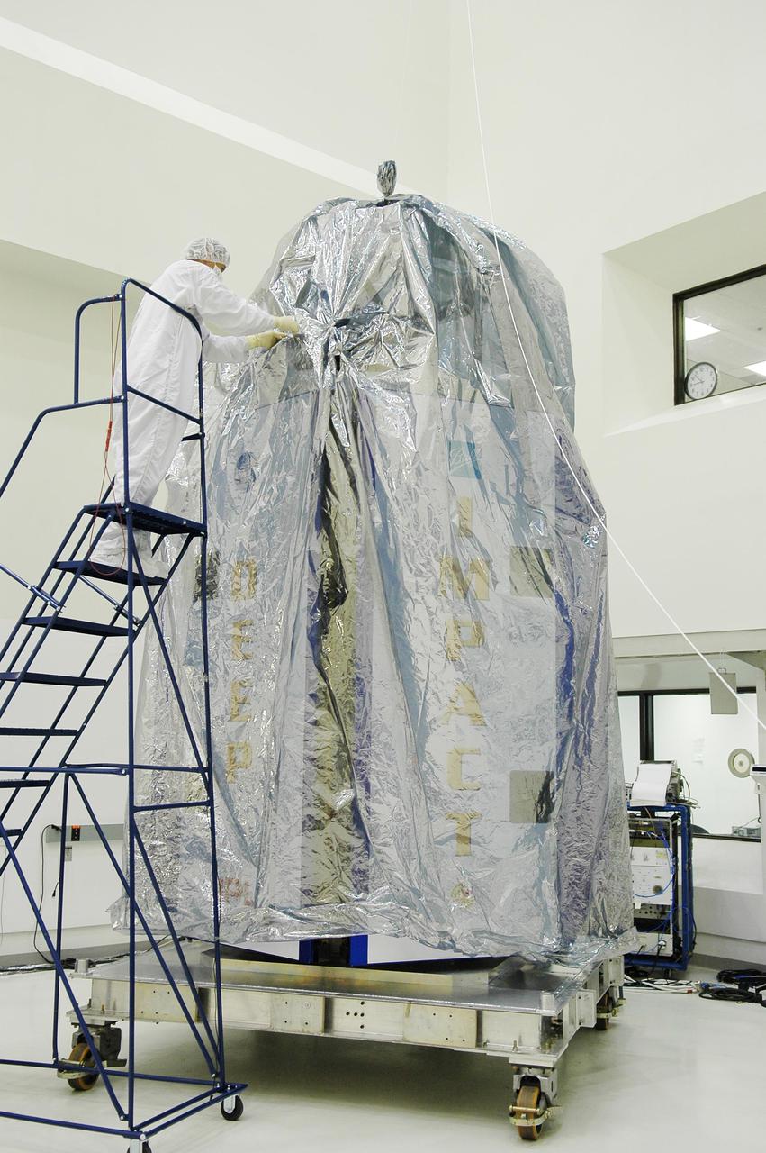 KENNEDY SPACE CENTER, FLA. -  At Astrotech Space Operations in Titusville, Fla., workers secure the protective cover around the Deep Impact spacecraft.  Deep Impact is being prepared for a move to the Hazardous Fuel Building and eventually shipment to Launch Pad 17-B, Cape Canaveral Air Force Station.  At Astrotech Space Operations in Titusville, Fla., workers help guide an overhead crane holding a protective cover that will be placed over the Deep Impact spacecraft below. Deep Impact is being prepared for a move to the Hazardous Fuel Building and eventually shipment to Launch Pad 17-B, Cape Canaveral Air Force Station. Launch of Deep Impact is scheduled no earlier than Jan. 12.  A NASA Discovery mission, Deep Impact will probe beneath the surface of Comet Tempel 1 on July 4, 2005, when the comet is 83 million miles from Earth, and reveal the secrets of its interior.   After releasing a 3- by 3-foot projectile to crash onto the surface, Deep Impact’s flyby spacecraft will collect pictures and data of how the  crater forms, measuring the crater’s depth and diameter, as well as the composition of the interior of the crater and any material thrown out, and determining the changes in natural outgassing produced by the impact.  It will send the data back to Earth through the antennas of the Deep Space Network.