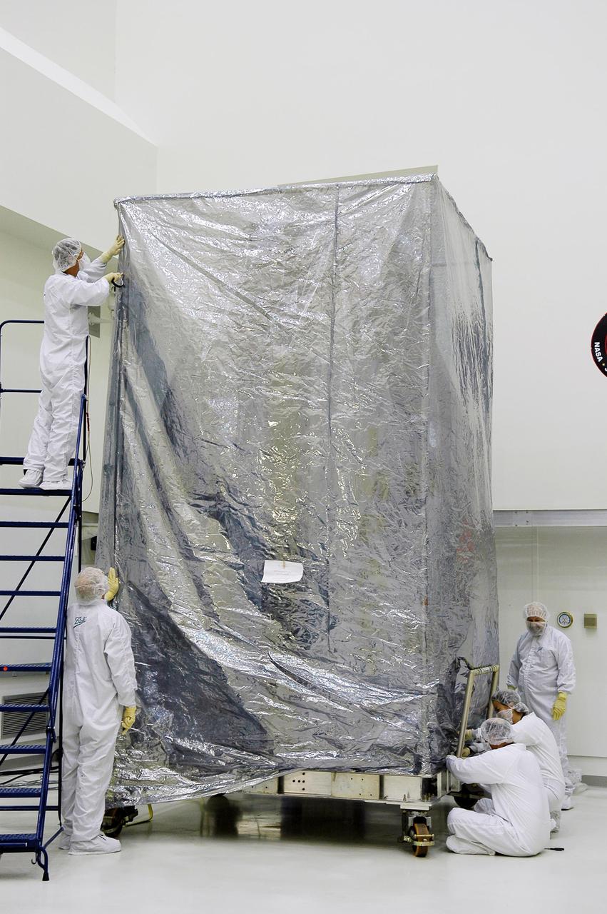 KENNEDY SPACE CENTER, FLA. -  At Astrotech Space Operations in Titusville, Fla., workers secure the second protective cover around the Deep Impact spacecraft.  Deep Impact is being prepared for a move to the Hazardous Fuel Building and eventually shipment to Launch Pad 17-B, Cape Canaveral Air Force Station.  At Astrotech Space Operations in Titusville, Fla., workers help guide an overhead crane holding a protective cover that will be placed over the Deep Impact spacecraft below. Deep Impact is being prepared for a move to the Hazardous Fuel Building and eventually shipment to Launch Pad 17-B, Cape Canaveral Air Force Station. Launch of Deep Impact is scheduled no earlier than Jan. 12.  A NASA Discovery mission, Deep Impact will probe beneath the surface of Comet Tempel 1 on July 4, 2005, when the comet is 83 million miles from Earth, and reveal the secrets of its interior.   After releasing a 3- by 3-foot projectile to crash onto the surface, Deep Impact’s flyby spacecraft will collect pictures and data of how the  crater forms, measuring the crater’s depth and diameter, as well as the composition of the interior of the crater and any material thrown out, and determining the changes in natural outgassing produced by the impact.  It will send the data back to Earth through the antennas of the Deep Space Network.