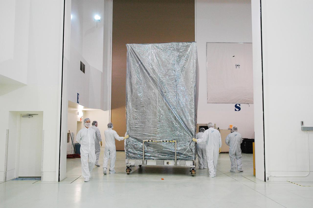 KENNEDY SPACE CENTER, FLA. -  At Astrotech Space Operations in Titusville, Fla., workers roll the Deep Impact spacecraft toward the door.  Deep Impact is being moved to the Hazardous Fuel Building and eventually shipment to Launch Pad 17-B, Cape Canaveral Air Force Station.  At Astrotech Space Operations in Titusville, Fla., workers help guide an overhead crane holding a protective cover that will be placed over the Deep Impact spacecraft below. Deep Impact is being prepared for a move to the Hazardous Fuel Building and eventually shipment to Launch Pad 17-B, Cape Canaveral Air Force Station. Launch of Deep Impact is scheduled no earlier than Jan. 12.  A NASA Discovery mission, Deep Impact will probe beneath the surface of Comet Tempel 1 on July 4, 2005, when the comet is 83 million miles from Earth, and reveal the secrets of its interior.   After releasing a 3- by 3-foot projectile to crash onto the surface, Deep Impact’s flyby spacecraft will collect pictures and data of how the  crater forms, measuring the crater’s depth and diameter, as well as the composition of the interior of the crater and any material thrown out, and determining the changes in natural outgassing produced by the impact.  It will send the data back to Earth through the antennas of the Deep Space Network.