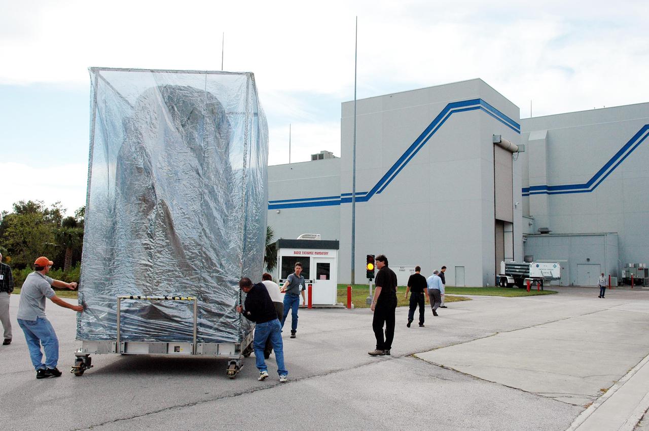 KENNEDY SPACE CENTER, FLA. -  At Astrotech Space Operations in Titusville, Fla., workers push the Deep Impact spacecraft toward the Hazardous Fuel Building.  Deep Impact is being prepared for shipment to Launch Pad 17-B, Cape Canaveral Air Force Station. At Astrotech Space Operations in Titusville, Fla., workers help guide an overhead crane holding a protective cover that will be placed over the Deep Impact spacecraft below. Deep Impact is being prepared for a move to the Hazardous Fuel Building and eventually shipment to Launch Pad 17-B, Cape Canaveral Air Force Station. Launch of Deep Impact is scheduled no earlier than Jan. 12.  A NASA Discovery mission, Deep Impact will probe beneath the surface of Comet Tempel 1 on July 4, 2005, when the comet is 83 million miles from Earth, and reveal the secrets of its interior.   After releasing a 3- by 3-foot projectile to crash onto the surface, Deep Impact’s flyby spacecraft will collect pictures and data of how the  crater forms, measuring the crater’s depth and diameter, as well as the composition of the interior of the crater and any material thrown out, and determining the changes in natural outgassing produced by the impact.  It will send the data back to Earth through the antennas of the Deep Space Network.