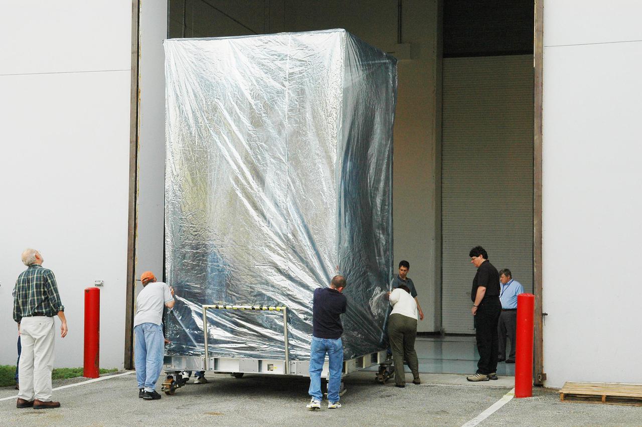 KENNEDY SPACE CENTER, FLA. -  At Astrotech Space Operations in Titusville, Fla., workers push the Deep Impact spacecraft into the Hazardous Fuel Building.  Deep Impact is being prepared for shipment to Launch Pad 17-B, Cape Canaveral Air Force Station. At Astrotech Space Operations in Titusville, Fla., workers help guide an overhead crane holding a protective cover that will be placed over the Deep Impact spacecraft below. Deep Impact is being prepared for a move to the Hazardous Fuel Building and eventually shipment to Launch Pad 17-B, Cape Canaveral Air Force Station. Launch of Deep Impact is scheduled no earlier than Jan. 12.  A NASA Discovery mission, Deep Impact will probe beneath the surface of Comet Tempel 1 on July 4, 2005, when the comet is 83 million miles from Earth, and reveal the secrets of its interior.   After releasing a 3- by 3-foot projectile to crash onto the surface, Deep Impact’s flyby spacecraft will collect pictures and data of how the  crater forms, measuring the crater’s depth and diameter, as well as the composition of the interior of the crater and any material thrown out, and determining the changes in natural outgassing produced by the impact.  It will send the data back to Earth through the antennas of the Deep Space Network.