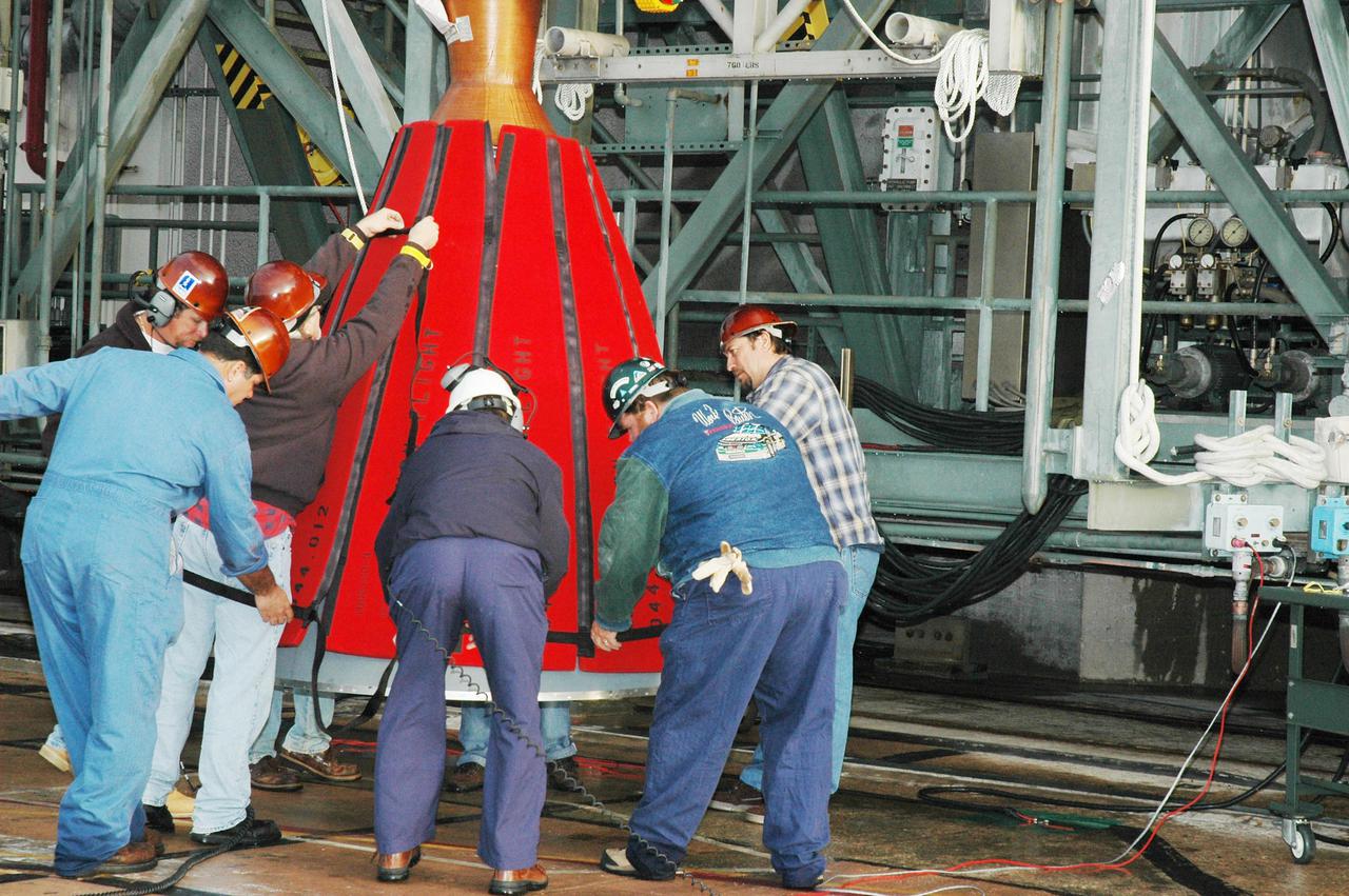 KENNEDY SPACE CENTER, FLA. -  At Launch Pad 17-B, Cape Canaveral Air Force Station, workers install a protective wrap on the Boeing Delta II second stage.  The component will be lifted up the mobile service tower and reattached to the interstage adapter on the Delta II.  The rocket is the launch vehicle for the Deep Impact spacecraft, scheduled for liftoff no earlier than Jan. 12.  A NASA Discovery mission, Deep Impact will probe beneath the surface of Comet Tempel 1 on July 4, 2005, when the comet is 83 million miles from Earth, and reveal the secrets of its interior.   After releasing a 3- by 3-foot projectile to crash onto the surface, Deep Impact’s flyby spacecraft will collect pictures and data of how the  crater forms, measuring the crater’s depth and diameter, as well as the composition of the interior of the crater and any material thrown out, and determining the changes in natural outgassing produced by the impact.  It will send the data back to Earth through the antennas of the Deep Space Network.