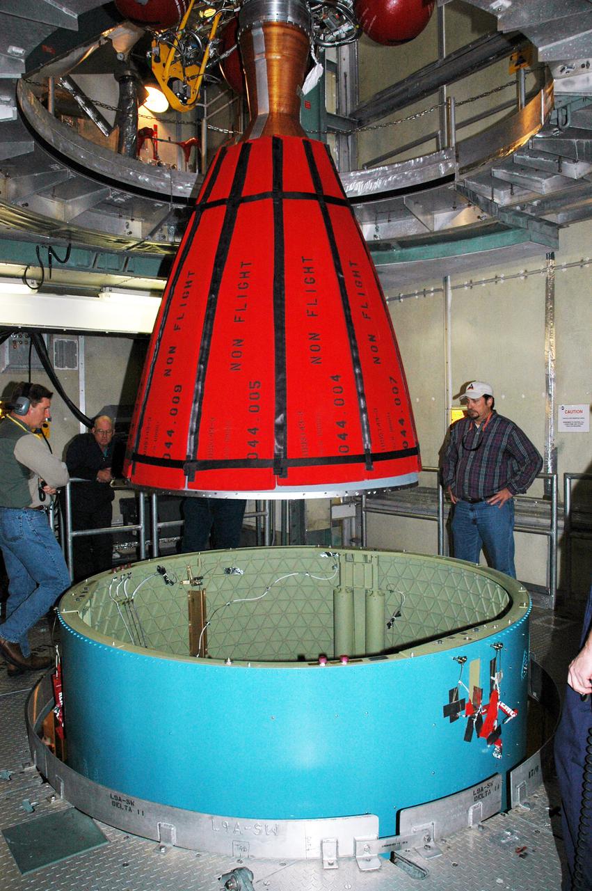 KENNEDY SPACE CENTER, FLA. -  Inside the mobile service tower on Launch Pad 17-B, Cape Canaveral Air Force Station, Boeing workers watch as the Delta II second stage is lowered toward the rocket below.  The component will be reattached to the interstage adapter on the Delta II.  The rocket is the launch vehicle for the Deep Impact spacecraft, scheduled for liftoff no earlier than Jan. 12.  A NASA Discovery mission, Deep Impact will probe beneath the surface of Comet Tempel 1 on July 4, 2005, when the comet is 83 million miles from Earth, and reveal the secrets of its interior.   After releasing a 3- by 3-foot projectile to crash onto the surface, Deep Impact’s flyby spacecraft will collect pictures and data of how the  crater forms, measuring the crater’s depth and diameter, as well as the composition of the interior of the crater and any material thrown out, and determining the changes in natural outgassing produced by the impact.  It will send the data back to Earth through the antennas of the Deep Space Network.