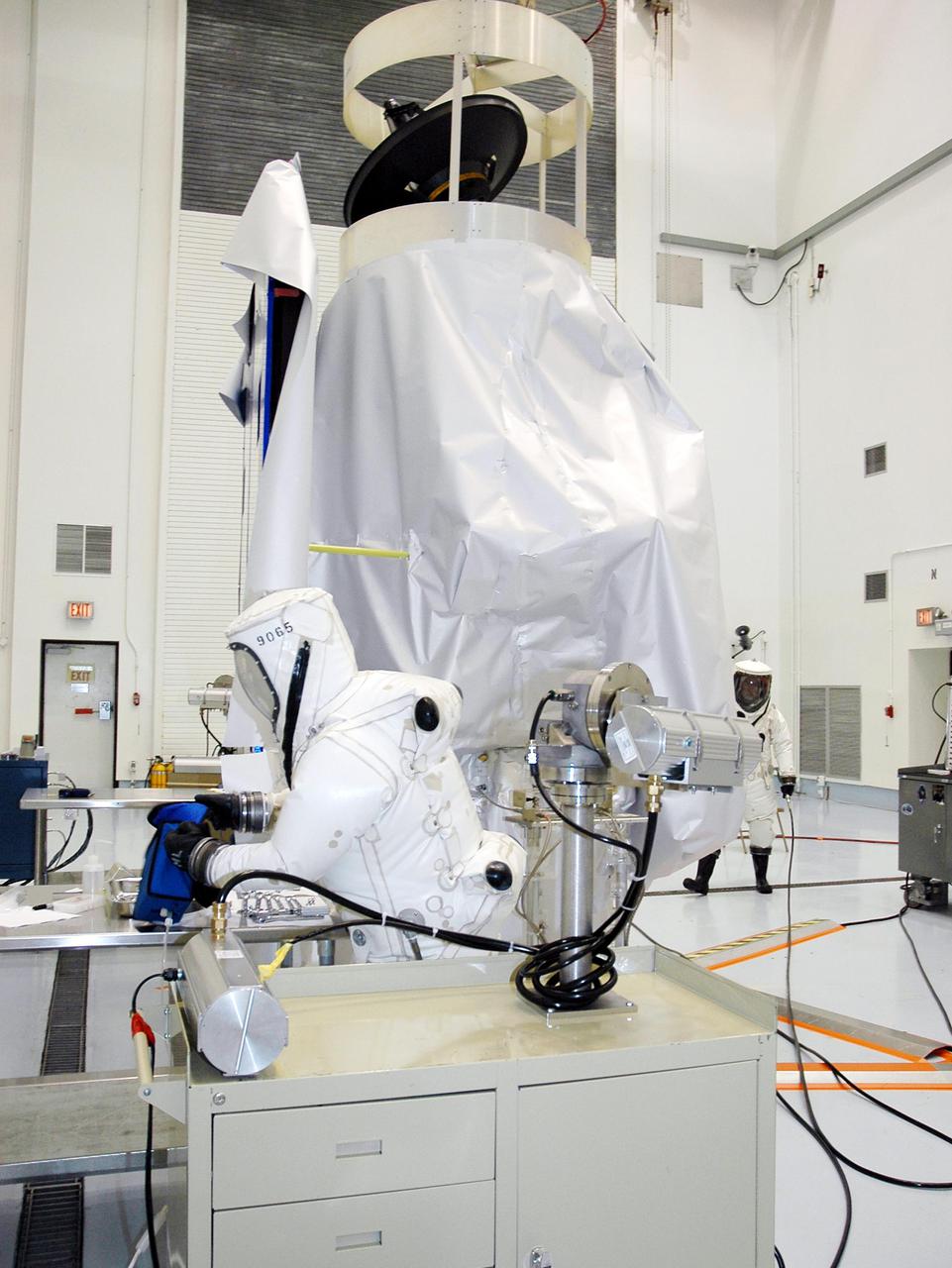 KENNEDY SPACE CENTER, FLA. -  Workers at Astrotech Space Operations in Titusville, Fla., get ready to begin fueling the Deep Impact spacecraft, seen wrapped in a protective cover in the background. Scheduled for liftoff Jan. 12,  Deep Impact will probe beneath the surface of Comet Tempel 1 on July 4, 2005, when the comet is 83 million miles from Earth, and reveal the secrets of its interior.   After releasing a 3- by 3-foot projectile to crash onto the surface, Deep Impact’s flyby spacecraft will collect pictures and data of how the  crater forms, measuring the crater’s depth and diameter, as well as the composition of the interior of the crater and any material thrown out, and determining the changes in natural outgassing produced by the impact.  It will send the data back to Earth through the antennas of the Deep Space Network.  Deep Impact is a NASA Discovery mission.
