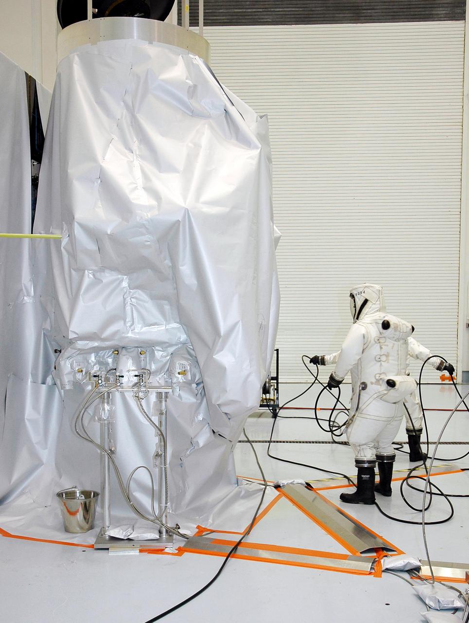 KENNEDY SPACE CENTER, FLA. -  Workers at Astrotech Space Operations in Titusville, Fla., get ready to begin fueling the Deep Impact spacecraft, seen wrapped in a protective cover in the background. Scheduled for liftoff Jan. 12,  Deep Impact will probe beneath the surface of Comet Tempel 1 on July 4, 2005, when the comet is 83 million miles from Earth, and reveal the secrets of its interior.   After releasing a 3- by 3-foot projectile to crash onto the surface, Deep Impact’s flyby spacecraft will collect pictures and data of how the  crater forms, measuring the crater’s depth and diameter, as well as the composition of the interior of the crater and any material thrown out, and determining the changes in natural outgassing produced by the impact.  It will send the data back to Earth through the antennas of the Deep Space Network.  Deep Impact is a NASA Discovery mission.