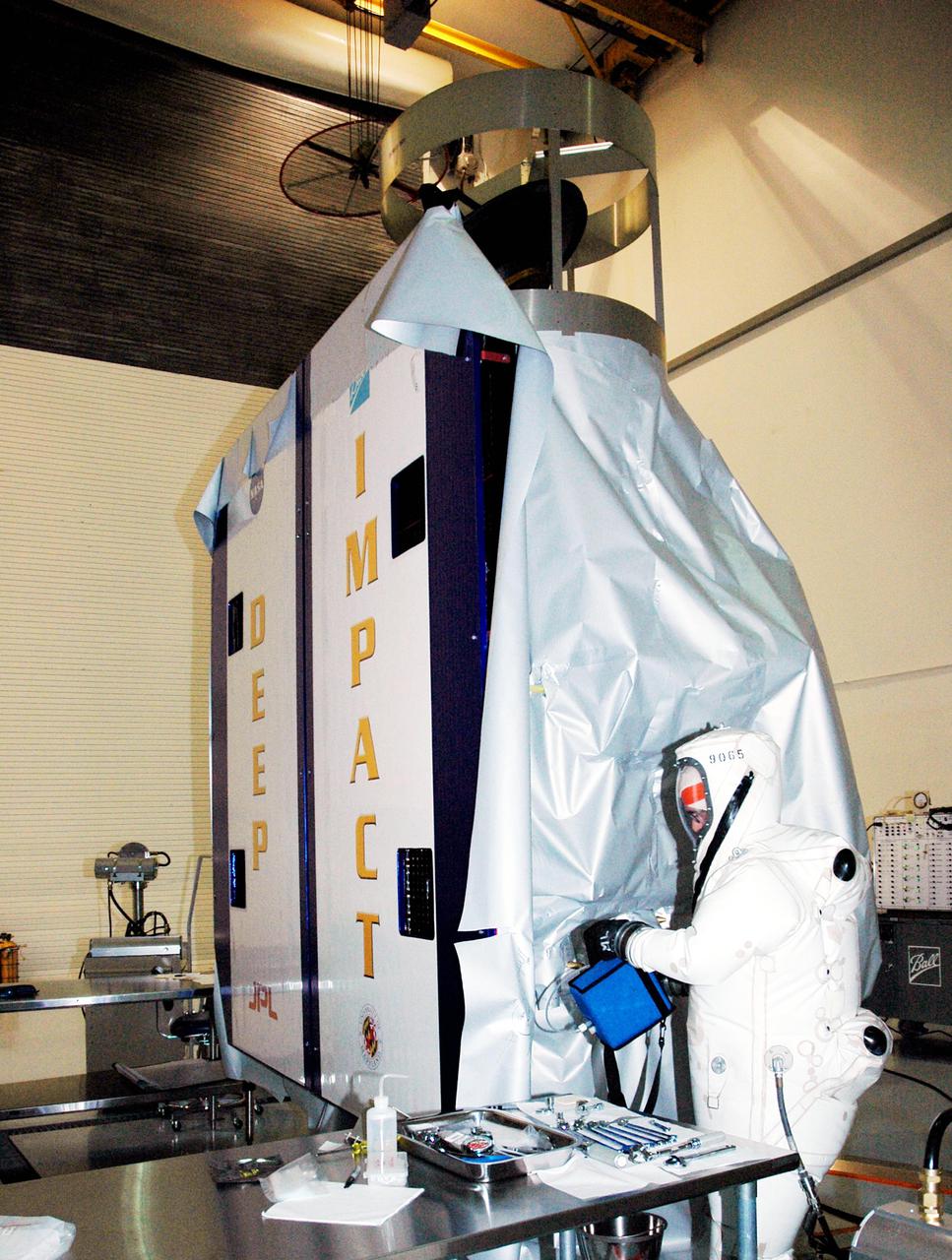 KENNEDY SPACE CENTER, FLA. -  A worker at Astrotech Space Operations in Titusville, Fla., begins fueling the Deep Impact spacecraft. Scheduled for liftoff Jan. 12,  Deep Impact will probe beneath the surface of Comet Tempel 1 on July 4, 2005, when the comet is 83 million miles from Earth, and reveal the secrets of its interior.   After releasing a 3- by 3-foot projectile to crash onto the surface, Deep Impact’s flyby spacecraft will collect pictures and data of how the  crater forms, measuring the crater’s depth and diameter, as well as the composition of the interior of the crater and any material thrown out, and determining the changes in natural outgassing produced by the impact.  It will send the data back to Earth through the antennas of the Deep Space Network.  Deep Impact is a NASA Discovery mission.