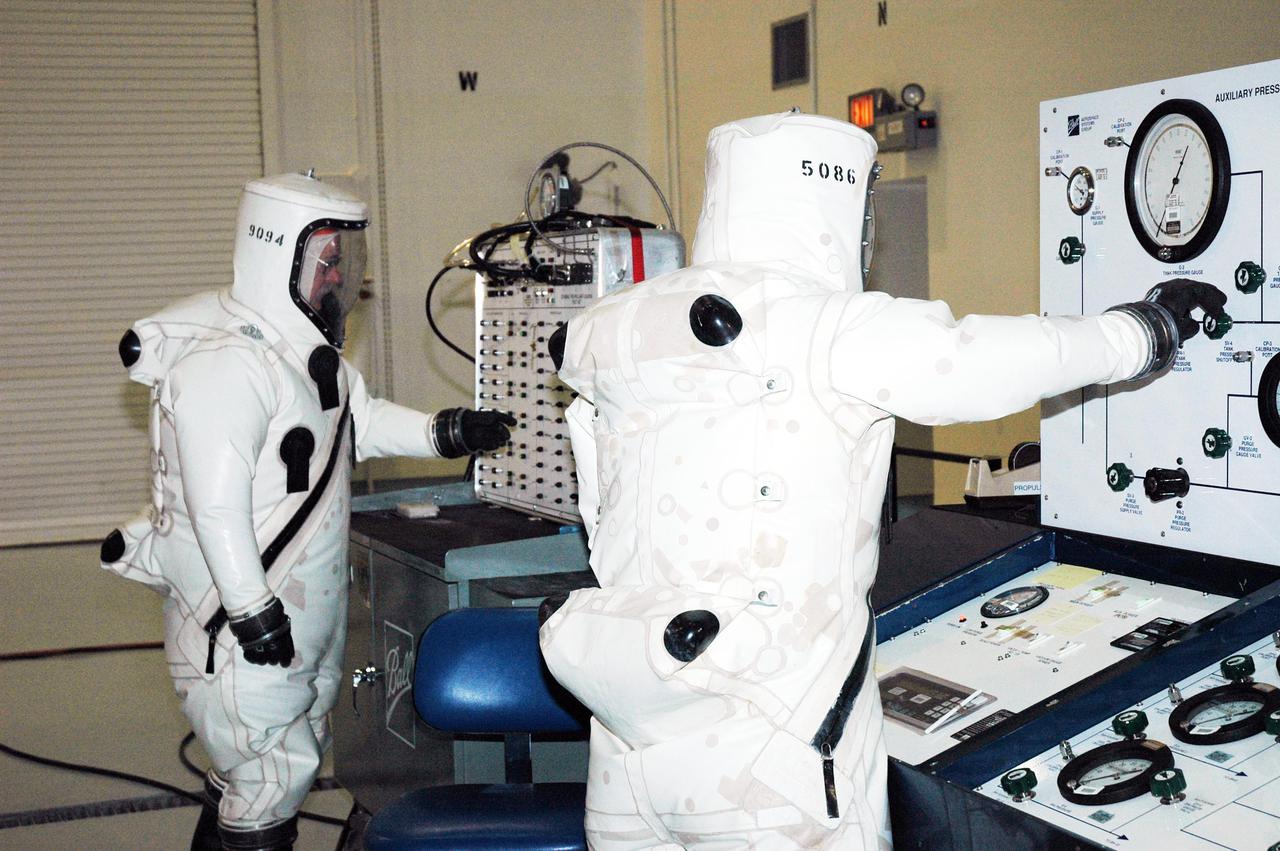 KENNEDY SPACE CENTER, FLA. -  Workers at Astrotech Space Operations in Titusville, Fla., check control panels during fueling of the Deep Impact spacecraft. Scheduled for liftoff Jan. 12,  Deep Impact will probe beneath the surface of Comet Tempel 1 on July 4, 2005, when the comet is 83 million miles from Earth, and reveal the secrets of its interior.   After releasing a 3- by 3-foot projectile to crash onto the surface, Deep Impact’s flyby spacecraft will collect pictures and data of how the  crater forms, measuring the crater’s depth and diameter, as well as the composition of the interior of the crater and any material thrown out, and determining the changes in natural outgassing produced by the impact.  It will send the data back to Earth through the antennas of the Deep Space Network.  Deep Impact is a NASA Discovery mission.