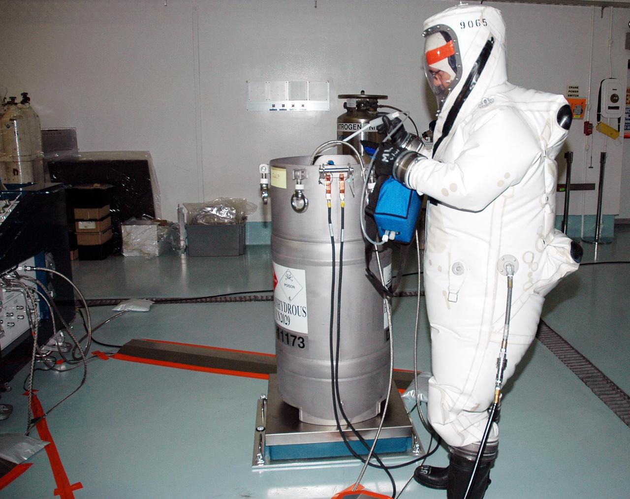 KENNEDY SPACE CENTER, FLA. -  Workers at Astrotech Space Operations in Titusville, Fla., begin fueling operations of the Deep Impact spacecraft, seen wrapped in a protective cover in the background. Scheduled for liftoff Jan. 12,  Deep Impact will probe beneath the surface of Comet Tempel 1 on July 4, 2005, when the comet is 83 million miles from Earth, and reveal the secrets of its interior.   After releasing a 3- by 3-foot projectile to crash onto the surface, Deep Impact’s flyby spacecraft will collect pictures and data of how the  crater forms, measuring the crater’s depth and diameter, as well as the composition of the interior of the crater and any material thrown out, and determining the changes in natural outgassing produced by the impact.  It will send the data back to Earth through the antennas of the Deep Space Network.  Deep Impact is a NASA Discovery mission.