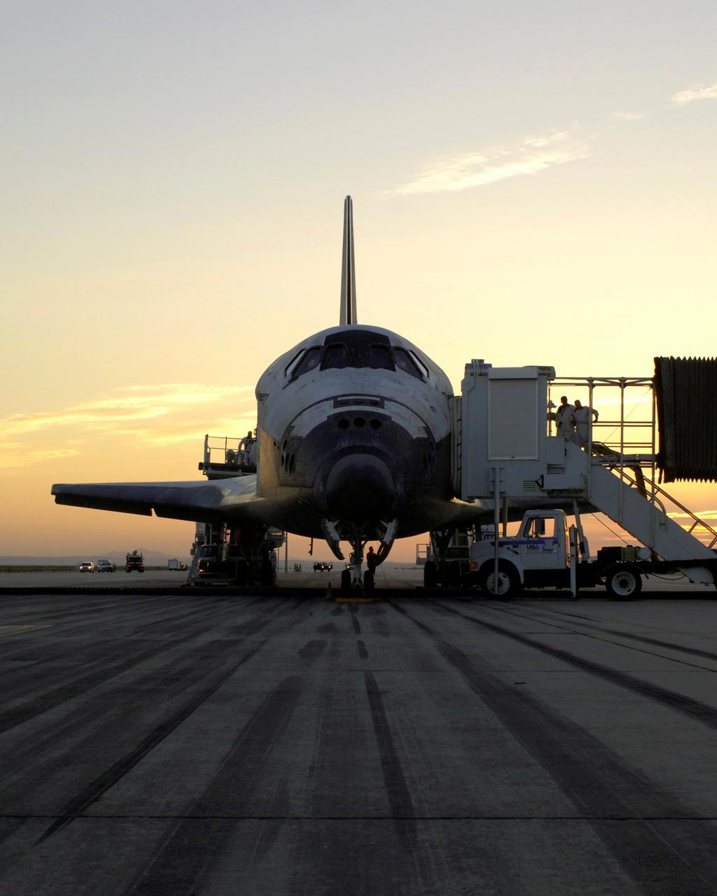 The sun rises on the Space Shuttle Discovery as it rests on the runway at Edward’s Air Force Base in California after a safe landing at 5:11 am (PDT) on August 9, 2005. The STS-114 landing concluded a historic 14 day return to flight mission to the International Space Station (ISS) after nearly a two and one half year delay in flight after the Space Shuttle Columbia tragedy in February 2003. Three successful space walks performed during the mission included a demonstration of repair techniques to the Shuttle’s thermal tiles known as the Thermal Protection System, the replacement of a failed Control Moment Gyroscope which helps keep the station oriented properly, and the installation of the External Stowage Platform, a space “shelf” for holding spare parts during Station construction. The shuttle’s heat shield repair was a first for Shuttle repair while still in space.