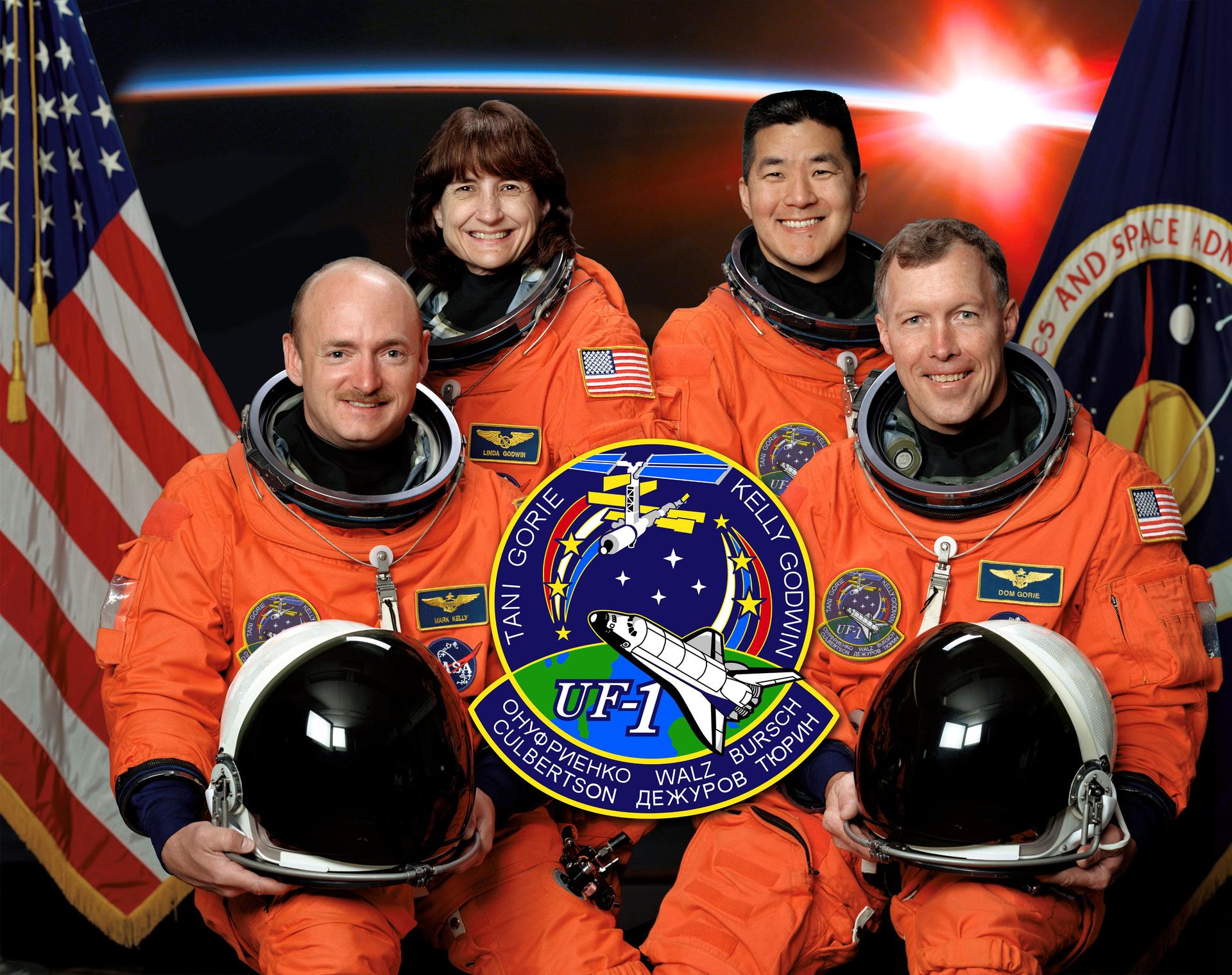 The STS-108 crew members take a break from their training to pose for their preflight portrait in orange spacesuits in front of flags.