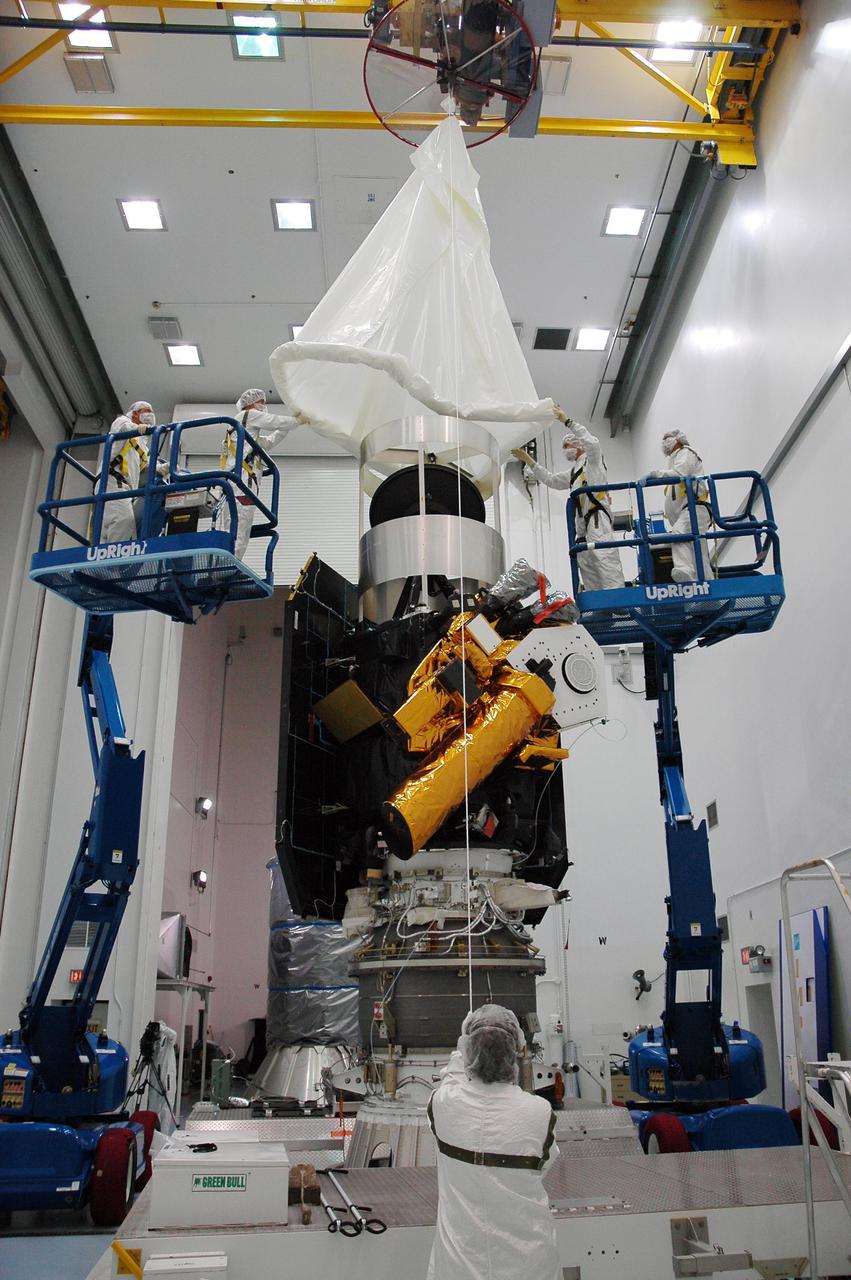 KENNEDY SPACE CENTER, FLA. - At Astrotech Space Operations in Titusville, Fla., a protective cover is being lowered over the Deep Impact spacecraft to protect it before the canister is installed around it. Once the spacecraft is completely covered, it will be transferred to Launch Pad 17-B on Cape Canaveral Air Force Station, Fla.  Then, in the mobile service tower, the fairing will be installed around the spacecraft.  The fairing is a molded structure that fits flush with the outside surface of the Delta II upper stage booster and forms an aerodynamically smooth joint, protecting the spacecraft during launch.  Scheduled for liftoff Jan. 12,  Deep Impact will probe beneath the surface of Comet Tempel 1 on July 4, 2005, when the comet is 83 million miles from Earth.  After releasing a 3- by 3-foot projectile to crash onto the surface, Deep Impact’s flyby spacecraft will reveal the secrets of its interior by collecting pictures and data of how the crater forms, measuring the crater’s depth and diameter as well as the composition of the interior of the crater and any material thrown out, and determining the changes in natural outgassing produced by the impact.  It will send the data back to Earth through the antennas of the Deep Space Network.  Deep Impact is a NASA Discovery mission.