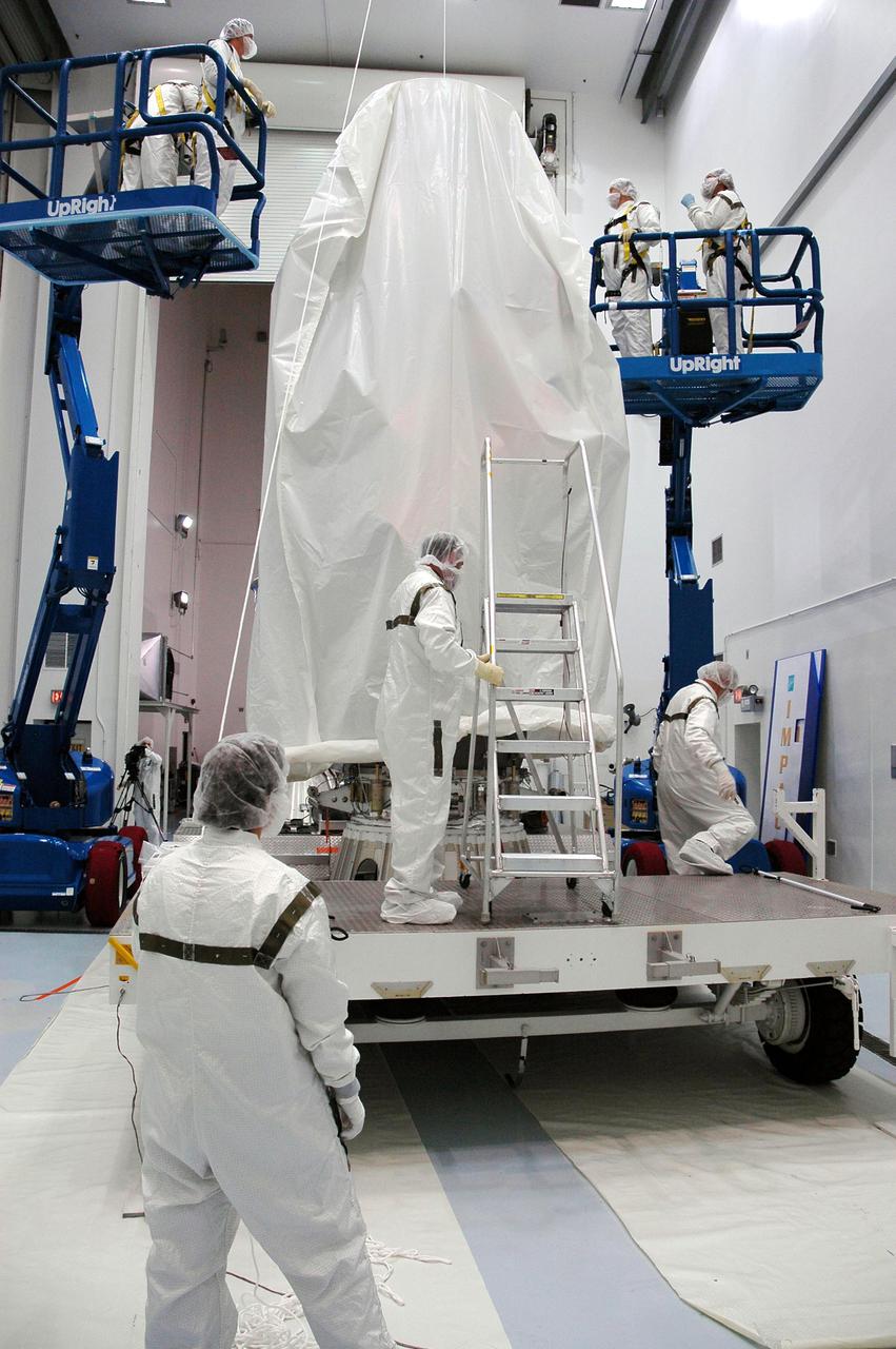 KENNEDY SPACE CENTER, FLA. - At Astrotech Space Operations in Titusville, Fla., Boeing technicians lower a protective cover over the Deep Impact spacecraft to protect it before the canister is installed around it. Once the spacecraft is completely covered, it will be transferred to Launch Pad 17-B on Cape Canaveral Air Force Station, Fla.  Then, in the mobile service tower, the fairing will be installed around the spacecraft.  The fairing is a molded structure that fits flush with the outside surface of the Delta II upper stage booster and forms an aerodynamically smooth joint, protecting the spacecraft during launch.  Scheduled for liftoff Jan. 12,  Deep Impact will probe beneath the surface of Comet Tempel 1 on July 4, 2005, when the comet is 83 million miles from Earth.  After releasing a 3- by 3-foot projectile to crash onto the surface, Deep Impact’s flyby spacecraft will reveal the secrets of its interior by collecting pictures and data of how the crater forms, measuring the crater’s depth and diameter as well as the composition of the interior of the crater and any material thrown out, and determining the changes in natural outgassing produced by the impact.  It will send the data back to Earth through the antennas of the Deep Space Network.  Deep Impact is a NASA Discovery mission.