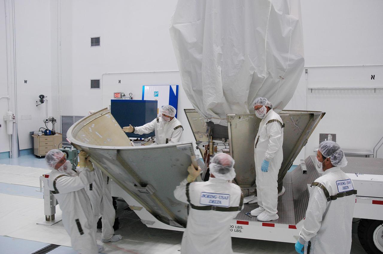 KENNEDY SPACE CENTER, FLA. - At Astrotech Space Operations in Titusville, Fla., Boeing technicians place the lower segments of a protective canister around the Deep Impact spacecraft. Once the spacecraft is completely covered, it will be transferred to Launch Pad 17-B on Cape Canaveral Air Force Station, Fla. Then, in the mobile service tower, the fairing will be installed around the spacecraft. The fairing is a molded structure that fits flush with the outside surface of the Delta II upper stage booster and forms an aerodynamically smooth joint, protecting the spacecraft during launch. Scheduled for liftoff Jan. 12, Deep Impact will probe beneath the surface of Comet Tempel 1 on July 4, 2005, when the comet is 83 million miles from Earth. After releasing a 3- by 3-foot projectile to crash onto the surface, Deep Impact’s flyby spacecraft will reveal the secrets of its interior by collecting pictures and data of how the crater forms, measuring the crater’s depth and diameter as well as the composition of the interior of the crater and any material thrown out, and determining the changes in natural outgassing produced by the impact. It will send the data back to Earth through the antennas of the Deep Space Network. Deep Impact is a NASA Discovery mission.