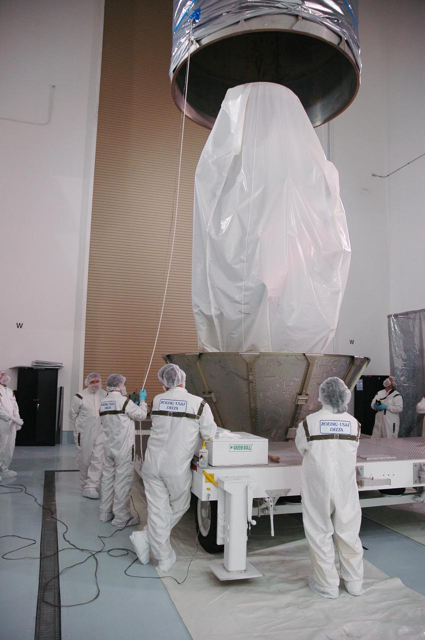 KENNEDY SPACE CENTER, FLA. - At Astrotech Space Operations in Titusville, Fla., technicians lower the upper canister toward the Deep Impact spacecraft.  It will be attached to the lower segments already surrounding the spacecraft. Once the spacecraft is completely covered, it will be transferred to Launch Pad 17-B on Cape Canaveral Air Force Station, Fla.  Then, in the mobile service tower, the fairing will be installed around the spacecraft.  The fairing is a molded structure that fits flush with the outside surface of the Delta II upper stage booster and forms an aerodynamically smooth joint, protecting the spacecraft during launch.  Scheduled for liftoff Jan. 12,  Deep Impact will probe beneath the surface of Comet Tempel 1 on July 4, 2005, when the comet is 83 million miles from Earth.  After releasing a 3- by 3-foot projectile to crash onto the surface, Deep Impact’s flyby spacecraft will reveal the secrets of its interior by collecting pictures and data of how the crater forms, measuring the crater’s depth and diameter as well as the composition of the interior of the crater and any material thrown out, and determining the changes in natural outgassing produced by the impact.  It will send the data back to Earth through the antennas of the Deep Space Network.  Deep Impact is a NASA Discovery mission.