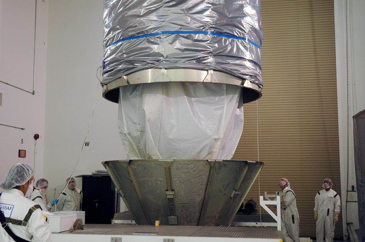 KENNEDY SPACE CENTER, FLA. - At Astrotech Space Operations in Titusville, Fla., technicians lower the upper canister toward the Deep Impact spacecraft.  It will be attached to the lower segments already surrounding the spacecraft. Once the spacecraft is completely covered, it will be transferred to Launch Pad 17-B on Cape Canaveral Air Force Station, Fla.  Then, in the mobile service tower, the fairing will be installed around the spacecraft.  The fairing is a molded structure that fits flush with the outside surface of the Delta II upper stage booster and forms an aerodynamically smooth joint, protecting the spacecraft during launch.  Scheduled for liftoff Jan. 12,  Deep Impact will probe beneath the surface of Comet Tempel 1 on July 4, 2005, when the comet is 83 million miles from Earth.  After releasing a 3- by 3-foot projectile to crash onto the surface, Deep Impact’s flyby spacecraft will reveal the secrets of its interior by collecting pictures and data of how the crater forms, measuring the crater’s depth and diameter as well as the composition of the interior of the crater and any material thrown out, and determining the changes in natural outgassing produced by the impact.  It will send the data back to Earth through the antennas of the Deep Space Network.  Deep Impact is a NASA Discovery mission.