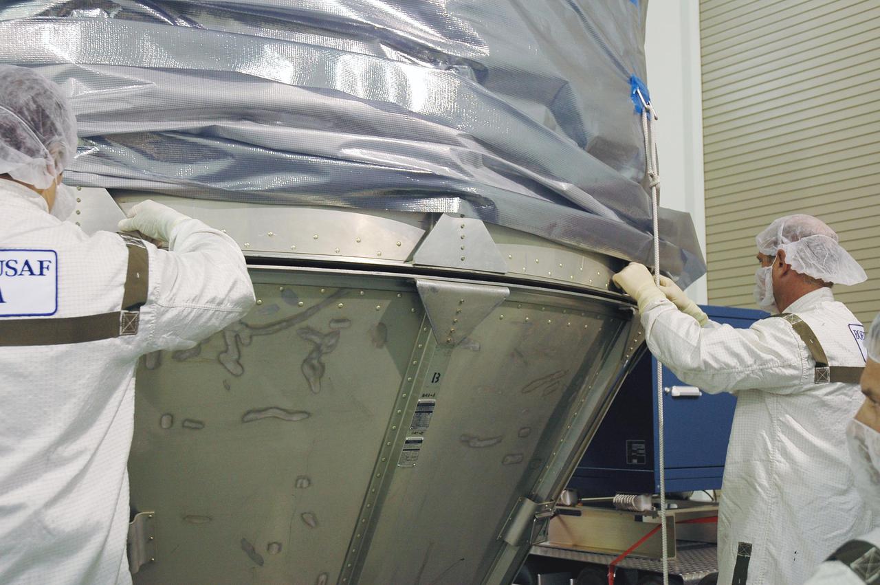 KENNEDY SPACE CENTER, FLA. - At Astrotech Space Operations in Titusville, Fla., Boeing technicians attach the upper canister with the lower segments surrounding the Deep Impact spacecraft. Once the spacecraft is completely covered, it will be transferred to Launch Pad 17-B on Cape Canaveral Air Force Station, Fla.  Then, in the mobile service tower, the fairing will be installed around the spacecraft.  The fairing is a molded structure that fits flush with the outside surface of the Delta II upper stage booster and forms an aerodynamically smooth joint, protecting the spacecraft during launch.  Scheduled for liftoff Jan. 12,  Deep Impact will probe beneath the surface of Comet Tempel 1 on July 4, 2005, when the comet is 83 million miles from Earth.  After releasing a 3- by 3-foot projectile to crash onto the surface, Deep Impact’s flyby spacecraft will reveal the secrets of its interior by collecting pictures and data of how the crater forms, measuring the crater’s depth and diameter as well as the composition of the interior of the crater and any material thrown out, and determining the changes in natural outgassing produced by the impact.  It will send the data back to Earth through the antennas of the Deep Space Network.  Deep Impact is a NASA Discovery mission.