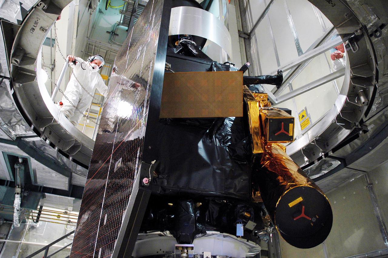 KENNEDY SPACE CENTER, FLA. - From a vantage point above, a worker observes the Deep Impact spacecraft exposed after removal of the canister and protective cover. Next the fairing will be installed around the spacecraft.  The fairing is a molded structure that fits flush with the outside surface of the Delta II upper stage booster and forms an aerodynamically smooth joint, protecting the spacecraft during launch and ascent.  Scheduled for liftoff Jan. 12,  Deep Impact will probe beneath the surface of Comet Tempel 1 on July 4, 2005, when the comet is 83 million miles from Earth.  After releasing a 3- by 3-foot projectile to crash onto the surface, Deep Impact’s flyby spacecraft will reveal the secrets of its interior by collecting pictures and data of how the crater forms, measuring the crater’s depth and diameter as well as the composition of the interior of the crater and any material thrown out, and determining the changes in natural outgassing produced by the impact.  It will send the data back to Earth through the antennas of the Deep Space Network.  Deep Impact is a NASA Discovery mission.
