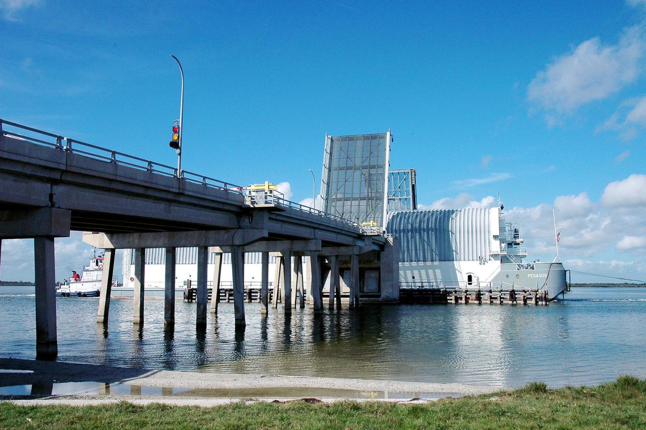 KENNEDY SPACE CENTER, FLA. - The tugboat towing the barge carrying the newly redesigned External Tank, designated for use on Return to Flight mission STS-114, passes through a drawbridge on its voyage to the Launch Complex 39 Area Turn Basin at Kennedy. The barge arrived after an approximately 900-mile journey at sea from the Michoud Assembly Facility in New Orleans. It left the facility Dec. 31 on the Pegasus, NASA’s specially designed barge, towed by Solid Rocket Booster retrieval ship Liberty Star. At Port Canaveral, the barge was then hooked up to the tugs for the last part of the journey to the Launch Complex 39 Area Turn Basin at Kennedy. Next, the External Tank will be off-loaded from the barge and transported to the Vehicle Assembly Building for its final checkout and mating to the twin Solid Rocket Boosters and orbiter Discovery. NASA and Lockheed Martin Corp. spent nearly two years modifying the 15-story, bronze-colored tank to make it safer for liftoff. Among dozens of changes is a redesigned forward bipod fitting -- a design that meets the recommendation of the Columbia Accident Investigation Board to reduce the risk to the Space Shuttle from falling debris during ascent. STS-114 is targeted for a launch opportunity beginning in May. The seven-member Discovery crew will fly to the International Space Station primarily to test and evaluate new procedures for flight safety, including Space Shuttle inspection and repair techniques.