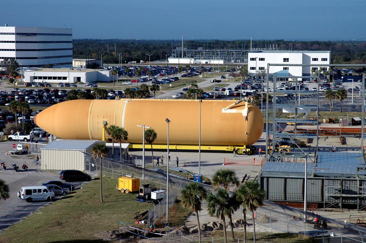 KENNEDY SPACE CENTER, FLA. - Viewed from the roof of the Launch Control Center in the Launch Complex 39 Area, the newly redesigned External Tank is seen moving along the roadway on its way to the Vehicle Assembly Building. In the background, at left, is the Operations Support Building I. In the transfer aisle of the VAB, the tank will be raised from a horizontal to a vertical position, then lifted high up into a storage cell, or “checkout cell,” where it will undergo inspections of the mechanical, electrical and thermal protection systems. New processing activities resulting from re-design of the tank include inspection of the bipod heater and External Tank separation camera, which includes charging the camera batteries. The tank will be then prepared for mating to the Solid Rocket Boosters. When preparations are complete, the tank will be lifted from the checkout cell, moved across the transfer aisle and into High Bay 1, where it will be lowered and attached to the boosters, which are sitting on the Mobile Launch Platform. The tank is designated for the Return to Flight mission, STS-114, targeted for a launch opportunity beginning in May. The seven-member Discovery crew will fly to the International Space Station primarily to test and evaluate new procedures for flight safety, including Space Shuttle inspection and repair techniques.