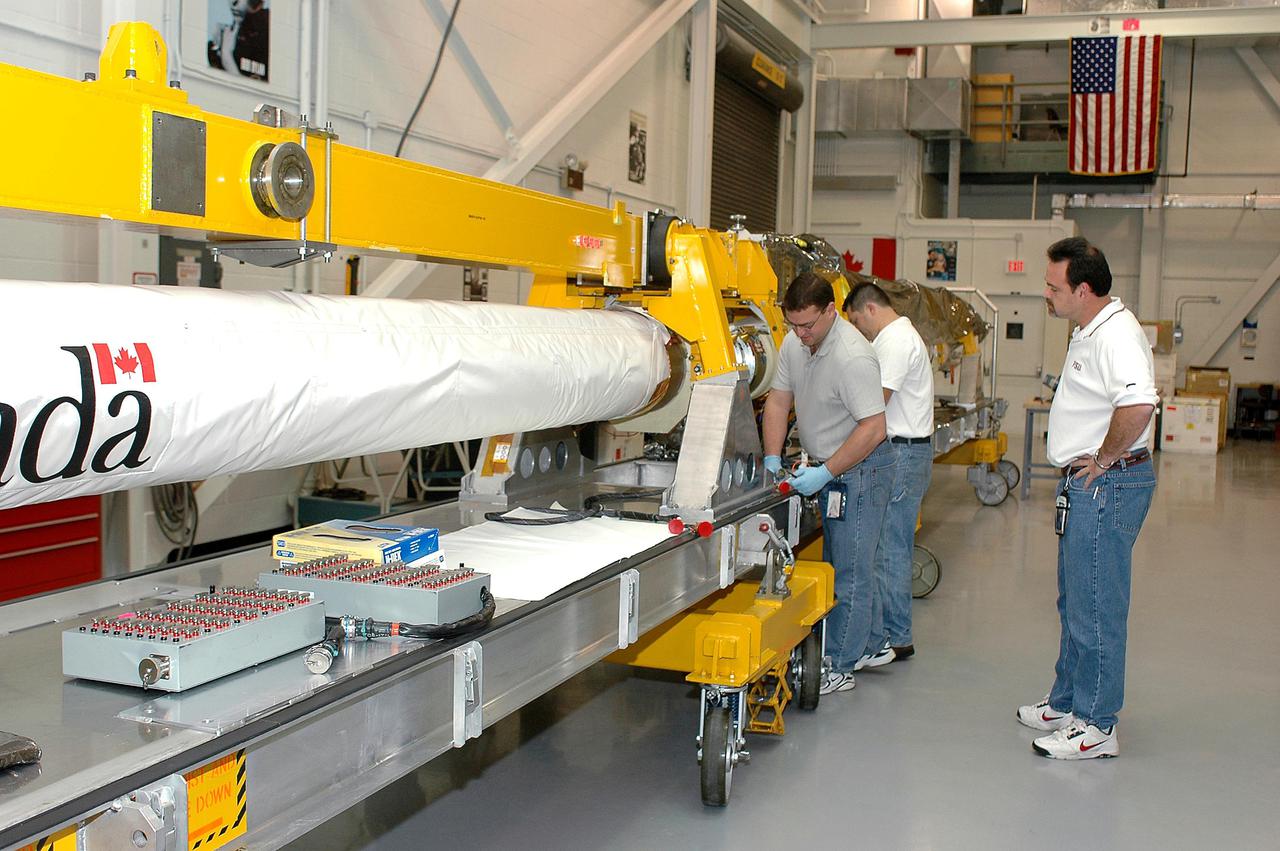 KENNEDY SPACE CENTER, FLA. - United Space Alliance technicians Todd Dugan and Jake Senior (at left) work on the Orbiter Boom Sensor System in the Remote Manipulator System lab while USA engineer Ron Kennedy (right) looks on. The OBSS is undergoing final checkout and testing in the lab prior to being transferred to the Orbiter Processing Facility for installation on Space Shuttle Discovery. The 50-foot-long OBSS will be attached to the Remote Manipulator System, or Shuttle arm, and is one of the new safety measures for Return to Flight, equipping the orbiter with cameras and laser systems to inspect the Shuttle's Thermal Protection System while in space. Discovery is slated to fly mission STS-114 once Space Shuttle launches resume. The launch planning window is May 12 to June 3, 2005.