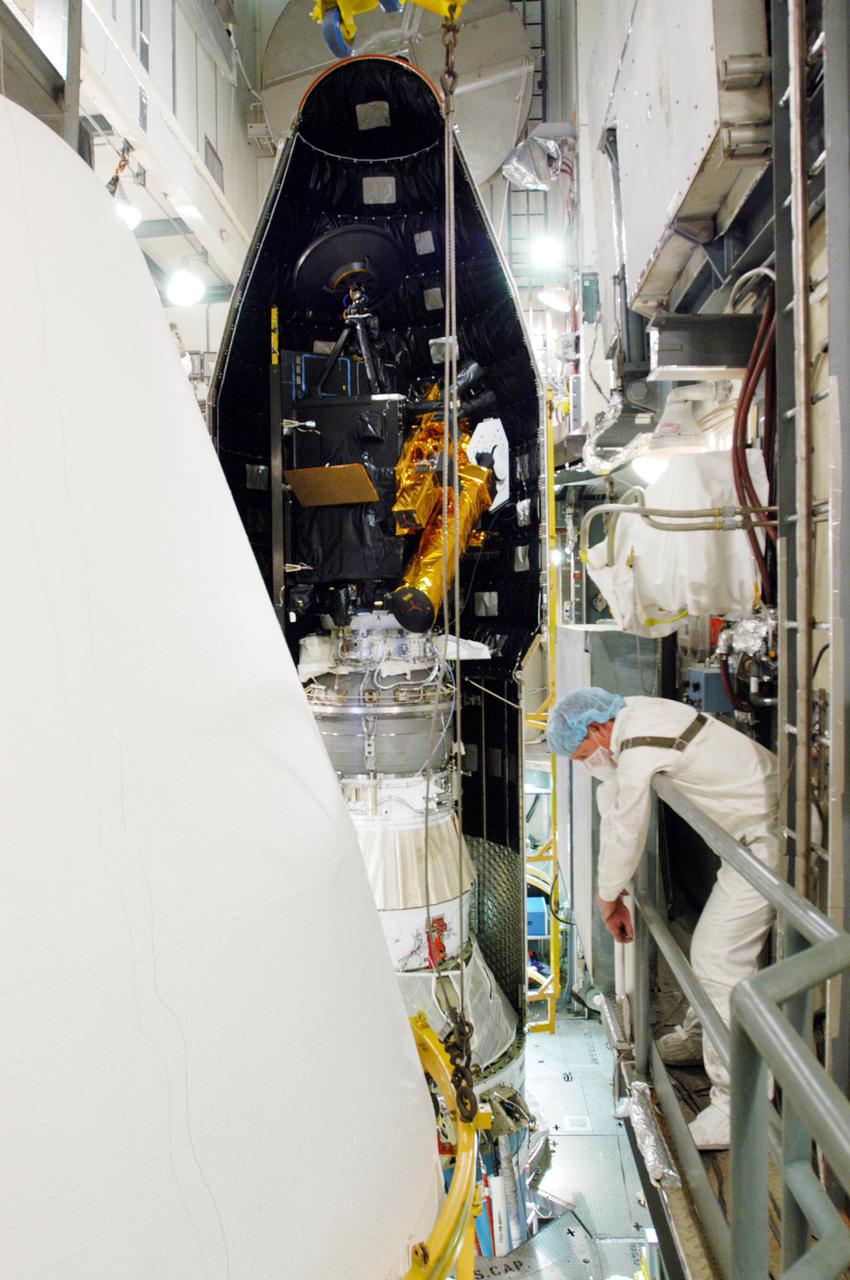 KENNEDY SPACE CENTER, FLA. - Inside the mobile service tower on Launch Pad 17-B, Cape Canaveral Air force Station, Fla., the partly enclosed Deep Impact spacecraft (background) waits while the second half of the fairing (foreground left) moves toward it. The fairing is a molded structure that fits flush with the outside surface of the Delta II upper stage booster and forms an aerodynamically smooth nosecone, protecting the spacecraft during launch and ascent. Scheduled for liftoff Jan. 12, Deep Impact will probe beneath the surface of Comet Tempel 1 on July 4, 2005, when the comet is 83 million miles from Earth. After releasing a 3- by 3-foot projectile to crash onto the surface, Deep Impact’s flyby spacecraft will reveal the secrets of its interior by collecting pictures and data of how the crater forms, measuring the crater’s depth and diameter as well as the composition of the interior of the crater and any material thrown out, and determining the changes in natural outgassing produced by the impact. It will send the data back to Earth through the antennas of the Deep Space Network. Deep Impact is a NASA Discovery mission.