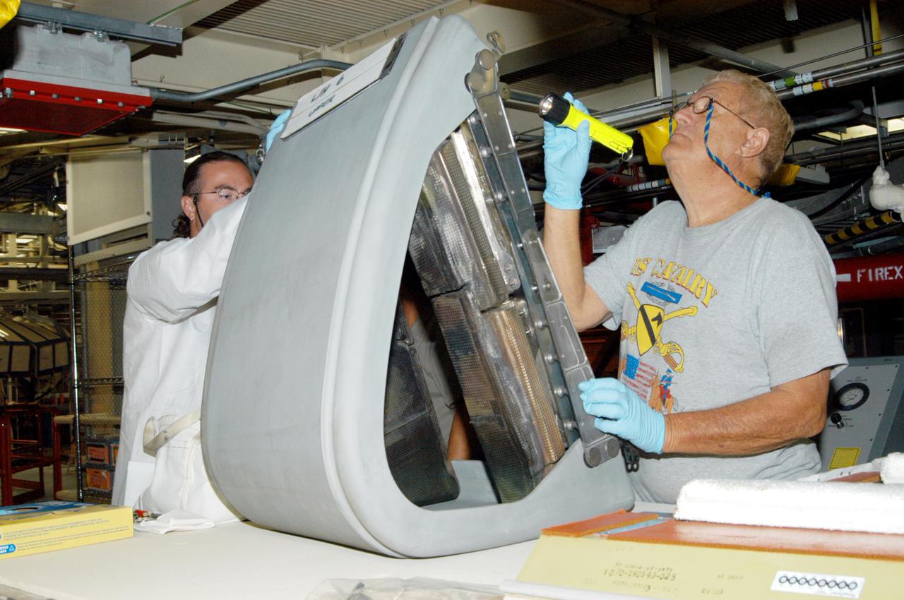 KENNEDY SPACE CENTER, FLA.  - In the Orbiter Processing Facility,  Matt Scott and Mel Romans (left and right), with United Space Alliance, closely inspect the final Reinforced Carbon-Carbon (RCC) panel to be installed on orbiter Discovery’s left wing.  The leading edges of each of an orbiter’s wings have 22 RCC panels. They are light gray and made entirely of carbon composite material, which protect the orbiter during re-entry. The molded components are approximately 0.25- to 0.5-inch thick and capable of withstanding temperatures up to 3,220 degrees F.  Following the Columbia accident in February 2002, which was caused by a breach in an RCC panel that allowed hot gases into the vehicle, each panel on Discovery was removed and thoroughly inspected before final reinstallation. Discovery is the designated orbiter to fly on the Return to Flight mission STS-114, the first Space Shuttle to launch since the accident.  The launch window for the mission is May 12 to June 3, 2005.