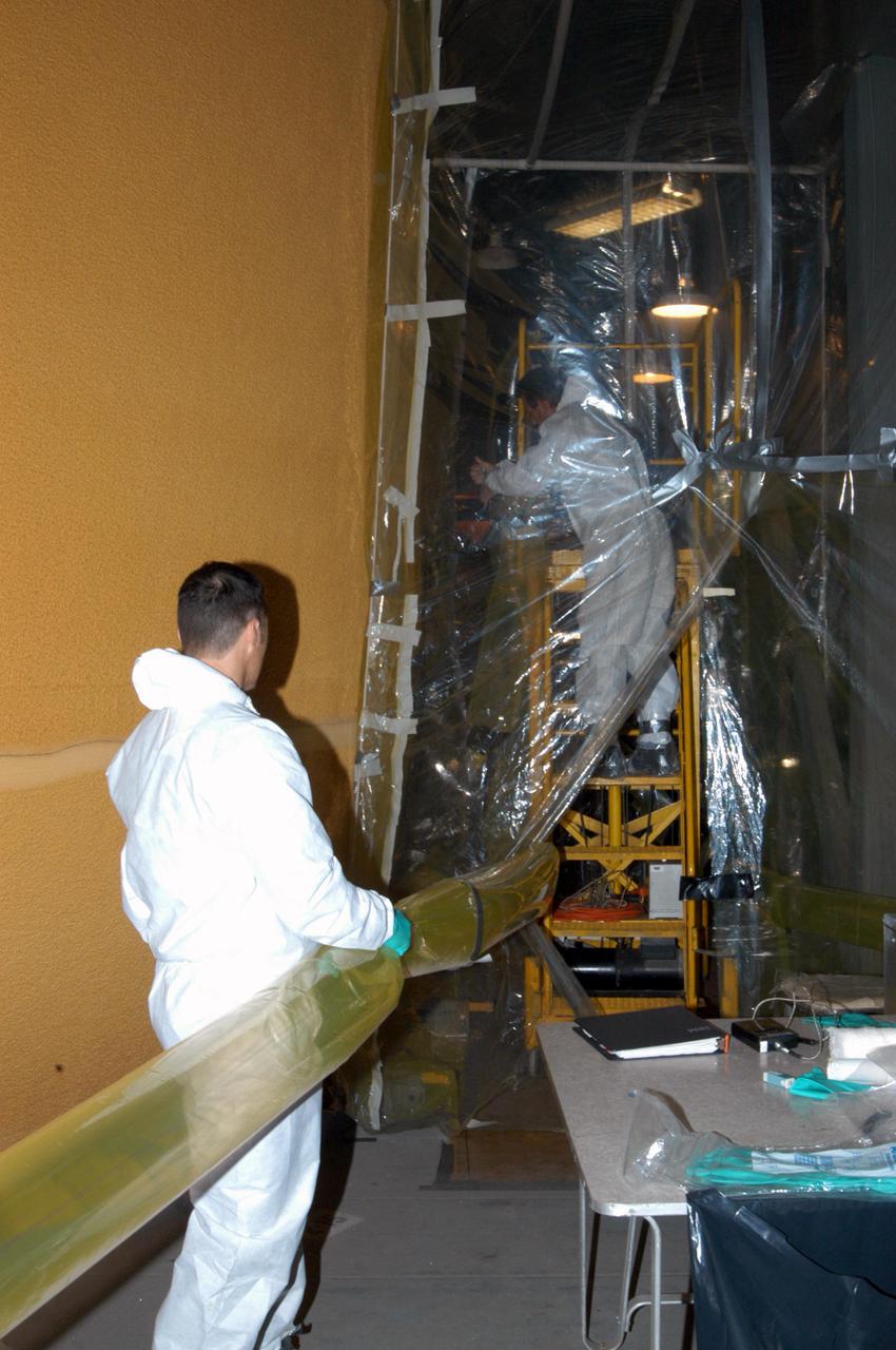 KENNEDY SPACE CENTER, FLA.  - In the Vehicle Assembly Building, United Space Alliance technicians Rob Williams (left) and Ed Carillion (background) work in the enclosure that is pumping warm, dry air around the External Tank (ET) to maintain the proper temperature and humidity prior to the aft hard-point closeout spray. The spray is being applied on an area of the tank where the ET is mated to the transporter.  Foam is not applied to that area at the Michoud Assembly Facility in Louisiana to avoid damage to the foam during travel.  The ET, which arrived at KSC Jan. 5, is in the checkout cell for final processing.  The tank is scheduled to fly on Space Shuttle Discovery on Return to Flight mission STS-114.  The launch window is May 12 to June 3.