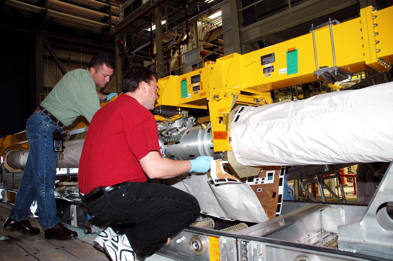 KENNEDY SPACE CENTER, FLA.  - In the back transfer aisle of the Orbiter Processing Facility bay 3, Todd Dugan (right), a technician with United Space Alliance, lifts a Thermal Protection System (TPS) blanket onto an area of the Orbiter Boom Sensor System (OBSS).  The installation will conclude TPS closeout prior to installation of the boom in the orbiter Discovery.  The OBSS is one of the new safety measures for Return to Flight, equipping the Shuttle with cameras and laser systems to inspect the Shuttle’s Thermal Protection System while in space.  Discovery is designated as the Return to Flight vehicle for mission STS-114, with a launch window of May 12 to June 3, 2005.