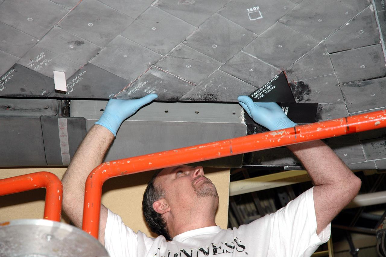 KENNEDY SPACE CENTER, FLA. - A worker in the Orbiter Processing Facility installs a new carrier panel on the orbiter Discovery. The new panel has an added thermal barrier that performs as a flow restrictor to further protect the wing leading edges. The panels fit between the Reinforced Carbon Carbon panel and the vehicle. The change is one of the safety features for return to flight. Discovery is the orbiter designated for the Return to Flight mission, STS-114. The launch window is May 12 to June 3, 2005.
