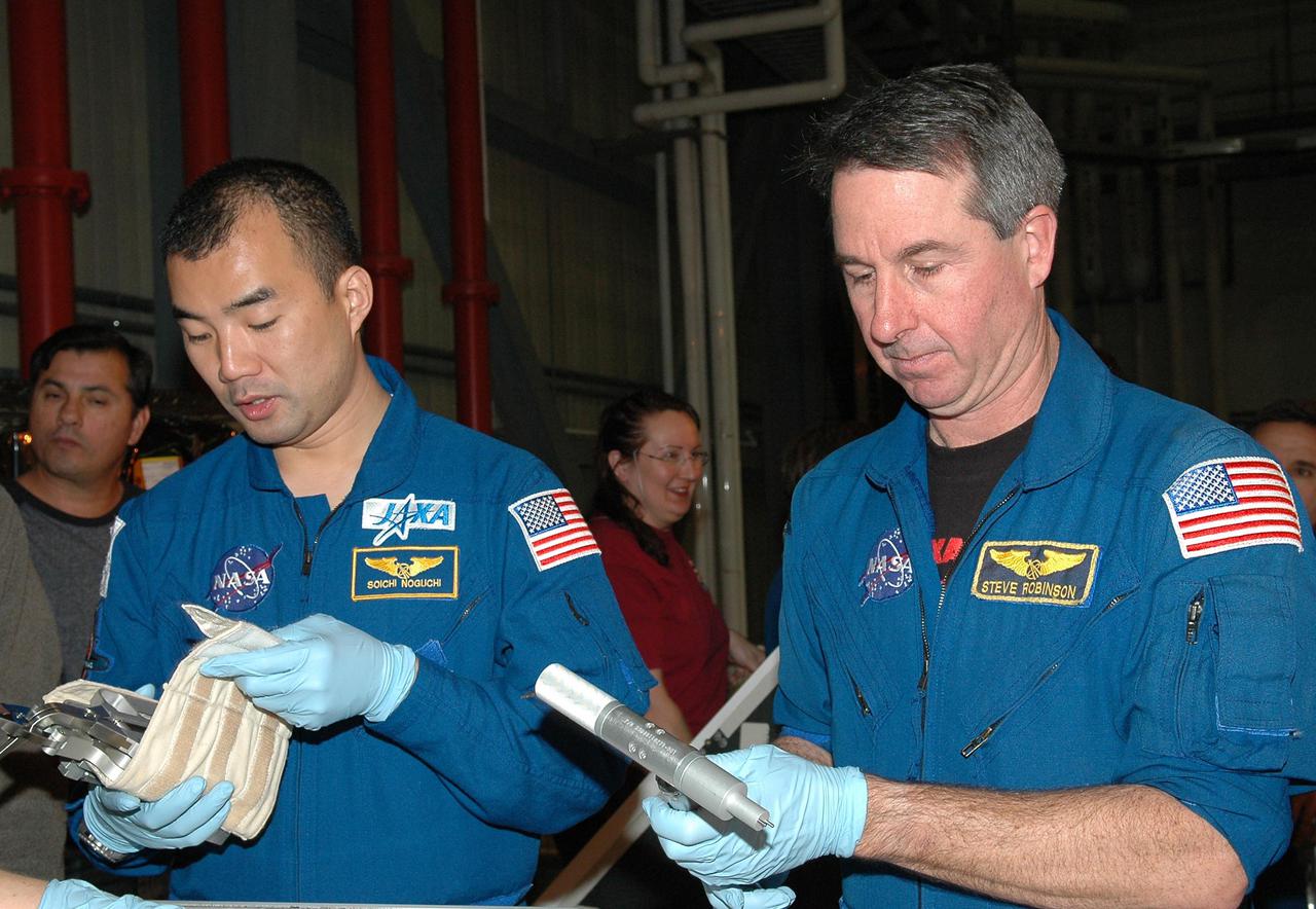KENNEDY SPACE CENTER, FLA.  - In the Orbiter Processing Facility, STS-114 Mission Specialists Soichi Noguchi (left) and Stephen Robinson look at tools from the Tool Stowage Assembly.  Robinson is holding the External Tank_umbilical door tool (one that is used if, during an EVA, an astronaut would have to manually close the ET Umbilical doors). The crew is at KSC for Crew Equipment Interface Test activities.  During CEIT, the crew has an opportunity to get a hands-on look at the payloads with which they’ll be working on orbit.  The Return to Flight mission STS-114 will carry a replacement Control Moment Gyroscope and the Multi-Purpose Logistics Module Raffaello, filled with supplies for the International Space Station.  Launch of STS-114 has a launch window of May 12 to June 3.