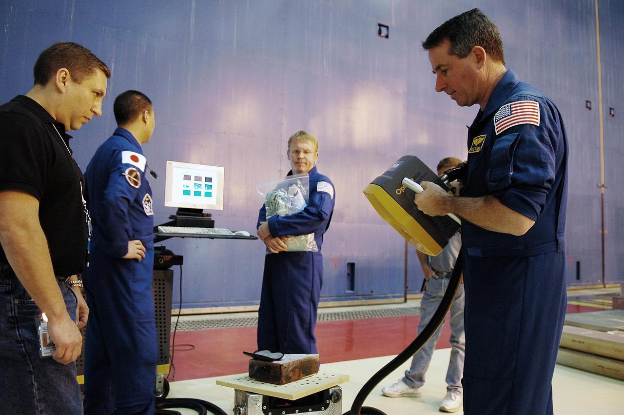 KENNEDY SPACE CENTER, FLA.  - In the Orbiter Processing Facility, STS-114 Mission Specialist Stephen Robinson (right, foreground) practices with a three-dimensional camera that will be used on future missions.  Other crew members watching are Mission Specialists Soichi Noguchi (second from left) and Andrew Thomas (center).  The crew is at KSC for Crew Equipment Interface Test activities.   During CEIT, the crew has an opportunity to get a hands-on look at the payloads with which they’ll be working on orbit.  The Return to Flight mission STS-114 will carry a replacement Control Moment Gyroscope and the Multi-Purpose Logistics Module Raffaello, filled with supplies for the International Space Station.  Launch of STS-114 has a launch window of May 12 to June 3.