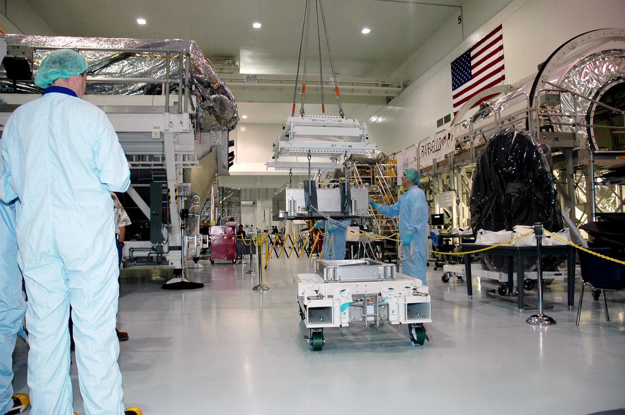 KENNEDY SPACE CENTER, FLA.  - Technicians at the Space Station Processing Facility carefully watch as a crane lifts the Thermal Protection System Detailed Test Objective (DTO) box.  It will be placed on the Lightweight Multi-Purpose Experiment Support Structure Carrier (LMC) to fly on Space Shuttle Discovery for mission STS-114. The DTO contains tile samples that will enable astronauts to test new on-orbit Thermal Protection System repair techniques.  The launch window for mission STS-114 is May 12 to June 3.