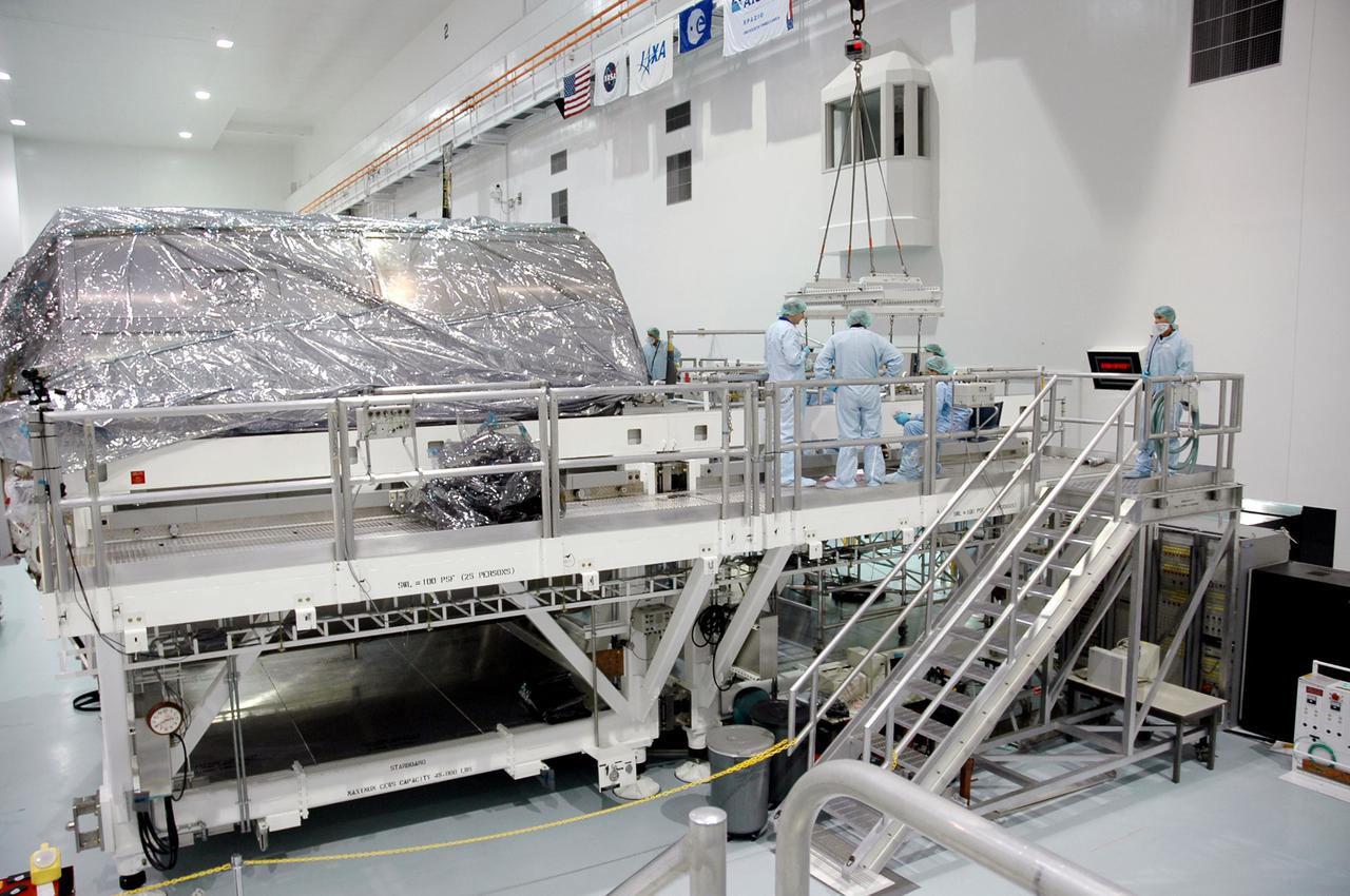 KENNEDY SPACE CENTER, FLA.  - Technicians in the Space Station Processing Facility check the placement of the Thermal Protection System Detailed Test Objective (DTO) box  on the Lightweight Multi-Purpose Experiment Support Structure Carrier (LMC).  The LMC and DTO will fly on Space Shuttle Discovery for mission STS-114.  The DTO contains tile samples that will enable astronauts to test new on-orbit Thermal Protection System repair techniques.  The launch window for mission STS-114 is May 12 to June 3.