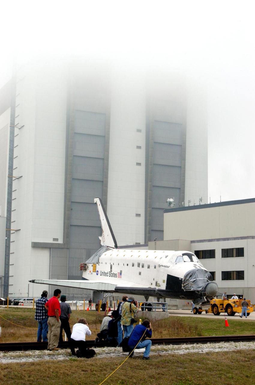 KENNEDY SPACE CENTER, FLA.  - Workers watch as the orbiter Endeavour rolls past the Vehicle Assembly Building on its way to Florida Space Authority’s Reusable Launch Vehicle hangar for temporary storage.  Endeavour is being moved from the Orbiter Processing Facility (OPF) to allow work to be performed in the OPF that can only be accomplished while the bay is empty.  Work scheduled in the OPF includes modifications to the bay and platform validation in the bay.   Endeavour will remain in the hangar for approximately 30 days, then return to the OPF.  Endeavour was pulled out of service in December 2003 for Orbiter Major Modification (OMM).  OMMs are scheduled at regular intervals to enhance safety and performance, infuse new technology, and, in this case, perform RTF modifications.