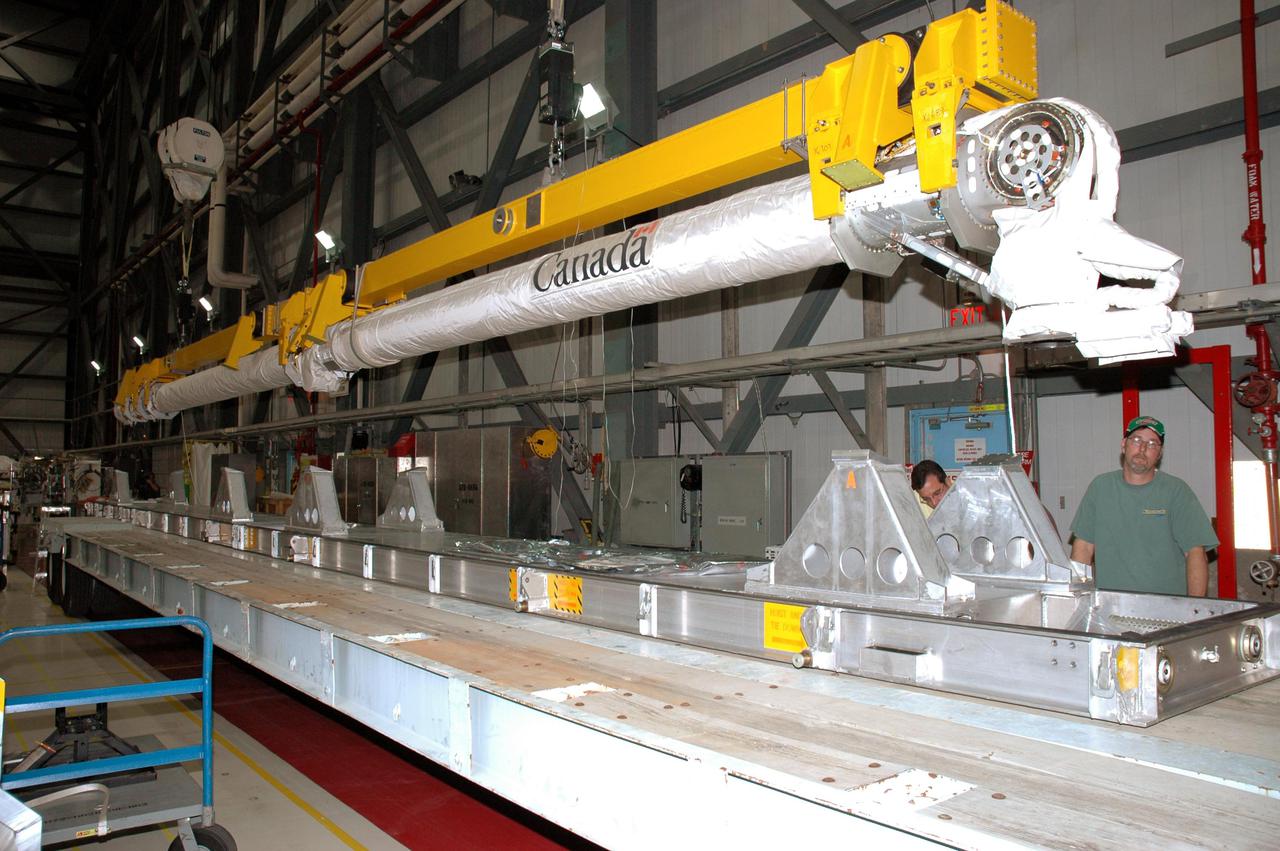 KENNEDY SPACE CENTER, FLA.  - In the Orbiter Processing Facility, an overhead crane moves the Remote Manipulator System (RMS), or Shuttle arm, toward Atlantis for installation in the payload bay.  The RMS includes the electromechanical arm that maneuvers a payload from the payload bay of the orbiter to its deployment position and then releases it. It can also grapple a free-flying payload, maneuver it to the payload bay of the orbiter and berth it in the orbiter. The RMS arm is 50 feet 3 inches long and 15 inches in diameter. It weighs 905 pounds, and the total system weighs 994 pounds. The RMS has six joints that correspond roughly to the joints of the human arm, with shoulder yaw and pitch joints; an elbow pitch joint; and wrist pitch, yaw and roll joints. The end effector is the unit at the end of the wrist that actually grabs, or grapples, the payload. Atlantis is the designated orbiter to fly on mission STS-121.  The mission has a launch window of July 12 - July 31, 2005.