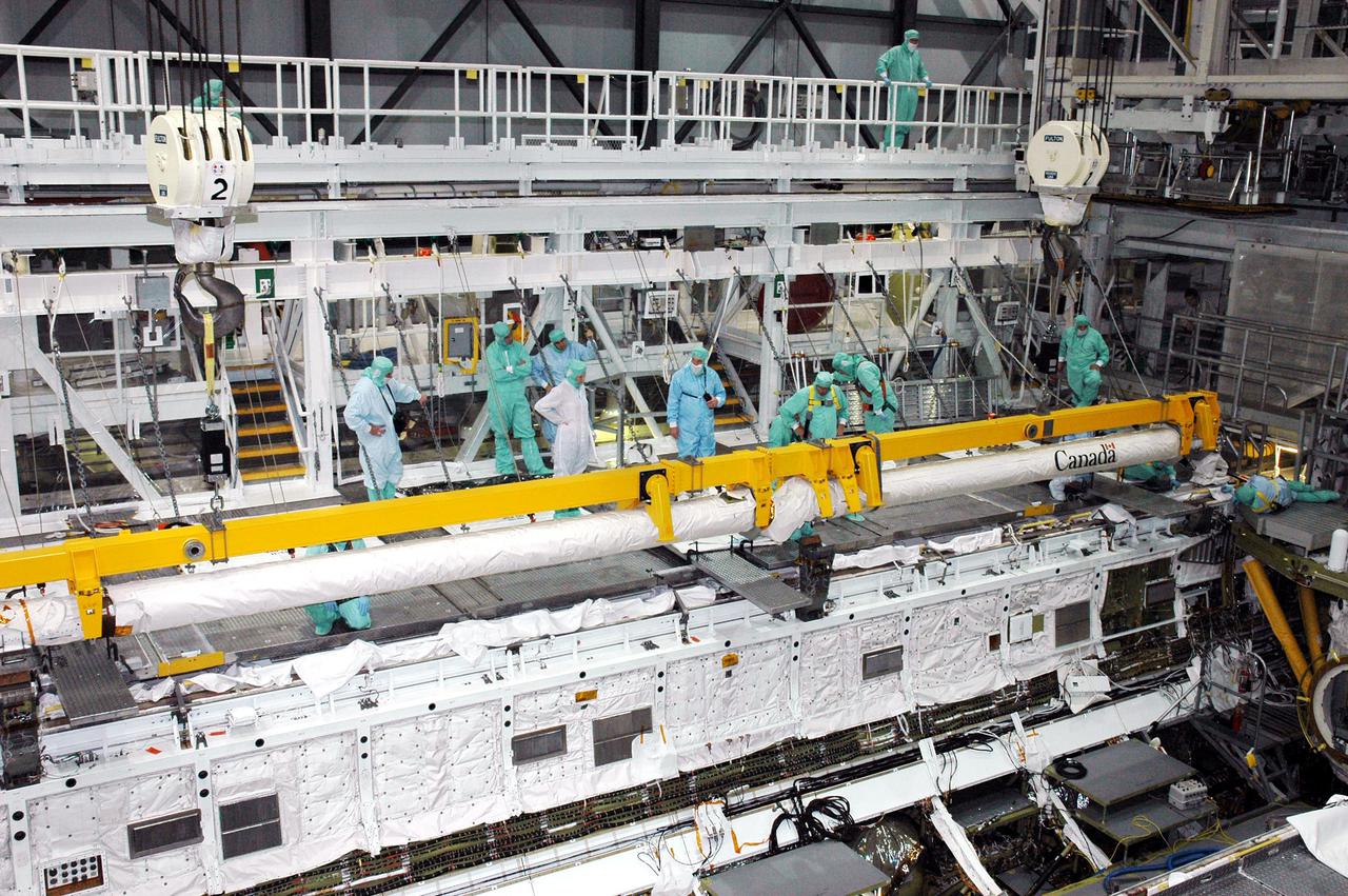 KENNEDY SPACE CENTER, FLA. - Workers in the Orbiter Processing Facility stand by as the Remote Manipulator System (RMS), or Shuttle arm, is lowered into place in Atlantis’ payload bay. The RMS includes the electromechanical arm that maneuvers a payload from the payload bay of the orbiter to its deployment position and then releases it. It can also grapple a free-flying payload, maneuver it to the payload bay of the orbiter and berth it in the orbiter. The RMS arm is 50 feet 3 inches long and 15 inches in diameter. It weighs 905 pounds, and the total system weighs 994 pounds. The RMS has six joints that correspond roughly to the joints of the human arm, with shoulder yaw and pitch joints; an elbow pitch joint; and wrist pitch, yaw and roll joints. The end effector is the unit at the end of the wrist that actually grabs, or grapples, the payload. Atlantis is the designated orbiter to fly on mission STS-121. The mission has a launch window of July 12 - July 31, 2005.
