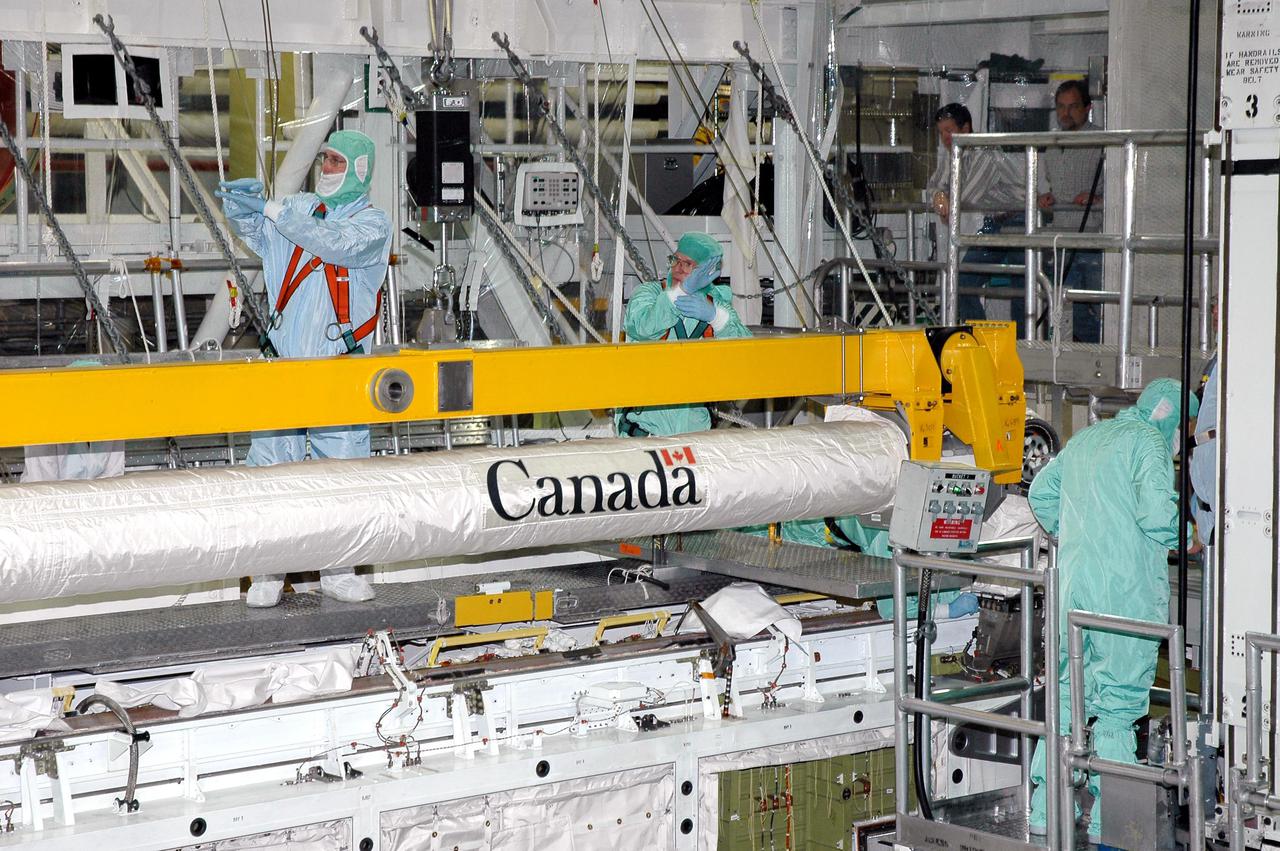 KENNEDY SPACE CENTER, FLA.  -  A worker in the Orbiter Processing Facility signals the crane operator to lower the Remote Manipulator System (RMS), or Shuttle arm, into place in Atlantis’ payload bay. The RMS includes the electromechanical arm that maneuvers a payload from the payload bay of the orbiter to its deployment position and then releases it. It can also grapple a free-flying payload, maneuver it to the payload bay of the orbiter and berth it in the orbiter.  The RMS arm is 50 feet 3 inches long and 15 inches in diameter. It weighs 905 pounds, and the total system weighs 994 pounds. The RMS has six joints that correspond roughly to the joints of the human arm, with shoulder yaw and pitch joints; an elbow pitch joint; and wrist pitch, yaw and roll joints. The end effector is the unit at the end of the wrist that actually grabs, or grapples, the payload. Atlantis is the designated orbiter to fly on mission STS-121.  The mission has a launch window of July 12 - July 31, 2005.