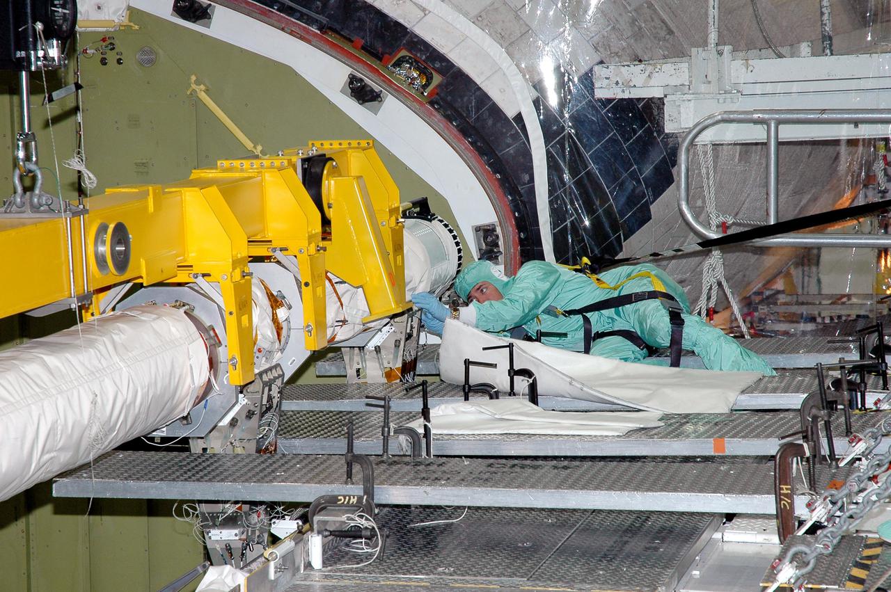 KENNEDY SPACE CENTER, FLA.  -  A worker in the Orbiter Processing Facility begins attaching the Remote Manipulator System (RMS), or Shuttle arm, into place in Atlantis’ payload bay. The RMS includes the electromechanical arm that maneuvers a payload from the payload bay of the orbiter to its deployment position and then releases it. It can also grapple a free-flying payload, maneuver it to the payload bay of the orbiter and berth it in the orbiter. The RMS arm is 50 feet 3 inches long and 15 inches in diameter. It weighs 905 pounds, and the total system weighs 994 pounds. The RMS has six joints that correspond roughly to the joints of the human arm, with shoulder yaw and pitch joints; an elbow pitch joint; and wrist pitch, yaw and roll joints. The end effector is the unit at the end of the wrist that actually grabs, or grapples, the payload. Atlantis is the designated orbiter to fly on mission STS-121.  The mission has a launch window of July 12 - July 31, 2005.