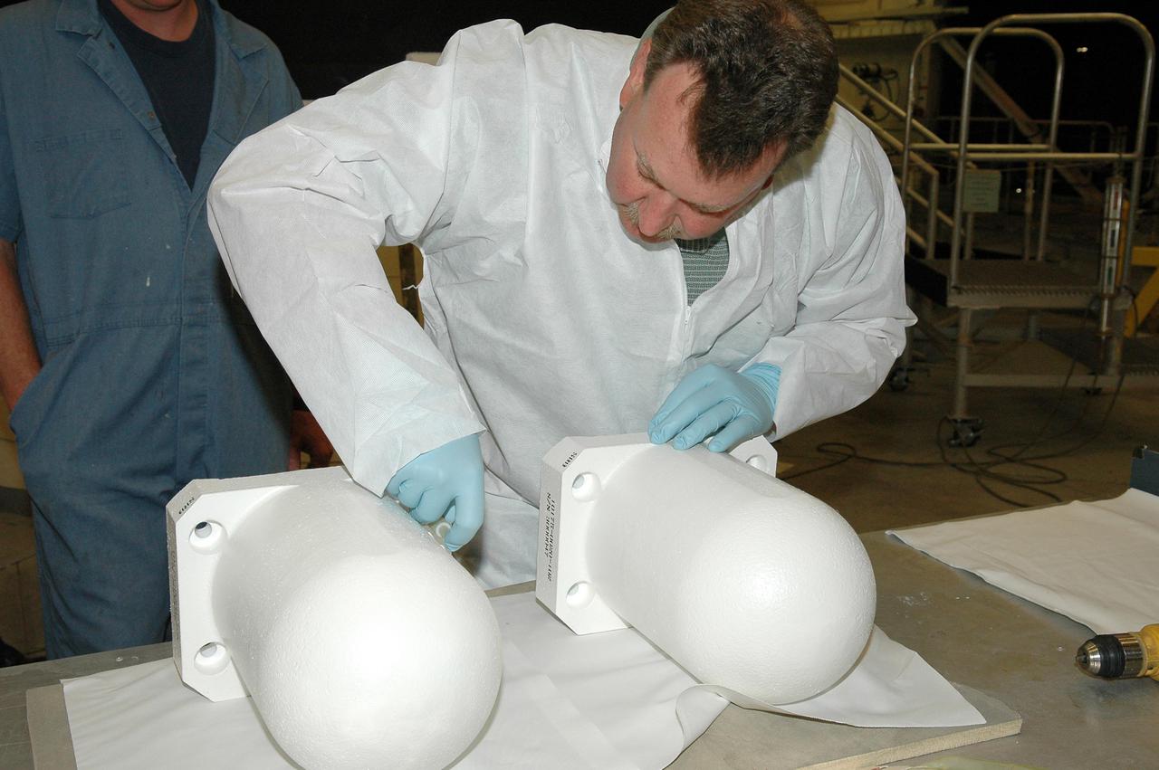 KENNEDY SPACE CENTER, FLA. - In the Vehicle Assembly Building, workers prepare these two bolt catchers for installation on orbiter Discovery’s External Tank. A bolt catcher is a vertical bolt mechanism at the forward end of the External Tank that attaches each booster to the tank. At approximately two minutes into launch, SRB separation begins when pyrotechnic devices fire to break the 25-inch, 62-pound steel bolts. One half of the bolt is caught in canister-like 'bolt catchers' located on the tank; the other half remains with the boosters. Discovery is flying with a modified bolt catcher, which was upgraded from a two-piece welded design to a one-piece, machine-made design as part of NASA's effort to return to safe, reliable spaceflight. Eliminating the weld makes a structurally stronger bolt catcher design. Though the bolt catcher is mounted on the External Tank, it is considered part of the Solid Rocket Booster element design. It is built by Summa Technologies, Inc. in Huntsville, Ala., insulated at Lockheed Martin’s Michoud Assembly Facility in New Orleans, and installed on the External Tank at KSC.