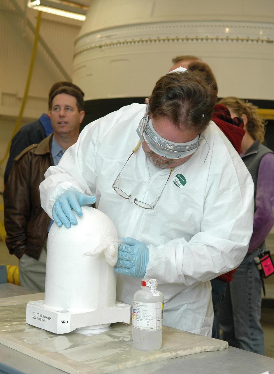 KENNEDY SPACE CENTER, FLA. - In the Vehicle Assembly Building, Senior Technician Kevin Reagan, with United Space Alliance, prepares one of two bolt catchers for installation on orbiter Discovery’s External Tank. A bolt catcher is a vertical bolt mechanism at the forward end of the External Tank that attaches each booster to the tank. At approximately two minutes into launch, SRB separation begins when pyrotechnic devices fire to break the 25-inch, 62-pound steel bolts. One half of the bolt is caught in canister-like 'bolt catchers' located on the tank; the other half remains with the boosters. Discovery is flying with a modified bolt catcher, which was upgraded from a two-piece welded design to a one-piece, machine-made design as part of NASA's effort to return to safe, reliable spaceflight. Eliminating the weld makes a structurally stronger bolt catcher design. Though the bolt catcher is mounted on the External Tank, it is considered part of the Solid Rocket Booster element design. It is built by Summa Technologies, Inc. in Huntsville, Ala., insulated at Lockheed Martin’s Michoud Assembly Facility in New Orleans, and installed on the External Tank at KSC.