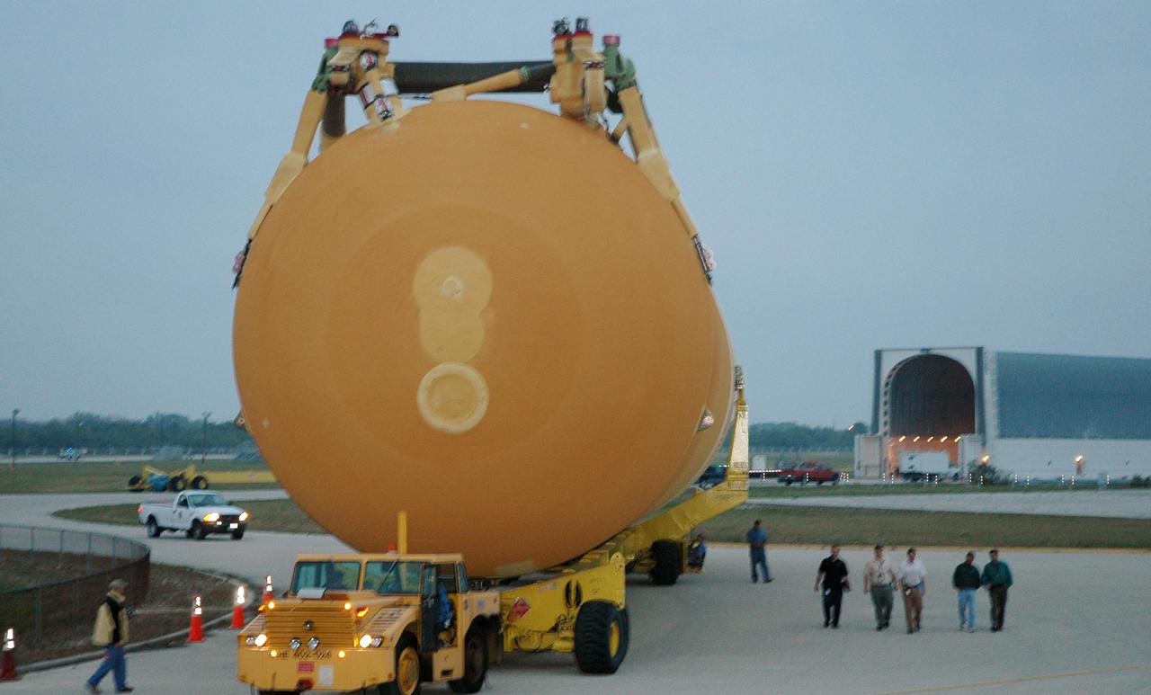 KENNEDY SPACE CENTER, FLA. - The second redesigned External Tank (ET-121) dwarfs the workers accompanying it on its way to the Vehicle Assembly Building. The tank recently arrived at the Turn Basin aboard the barge in the background after its 900-mile journey at sea from the Michoud Assembly Facility in New Orleans. In addition to the Return to Flight modifications, this tank has been outfitted with temperature sensors and accelerometers, used to measure vibration. These sensors will gather information about how the tank performs during flight. The tank is designated for use on Return to Flight mission STS-121, which has a launch window of July 12 to July 31, 2005.