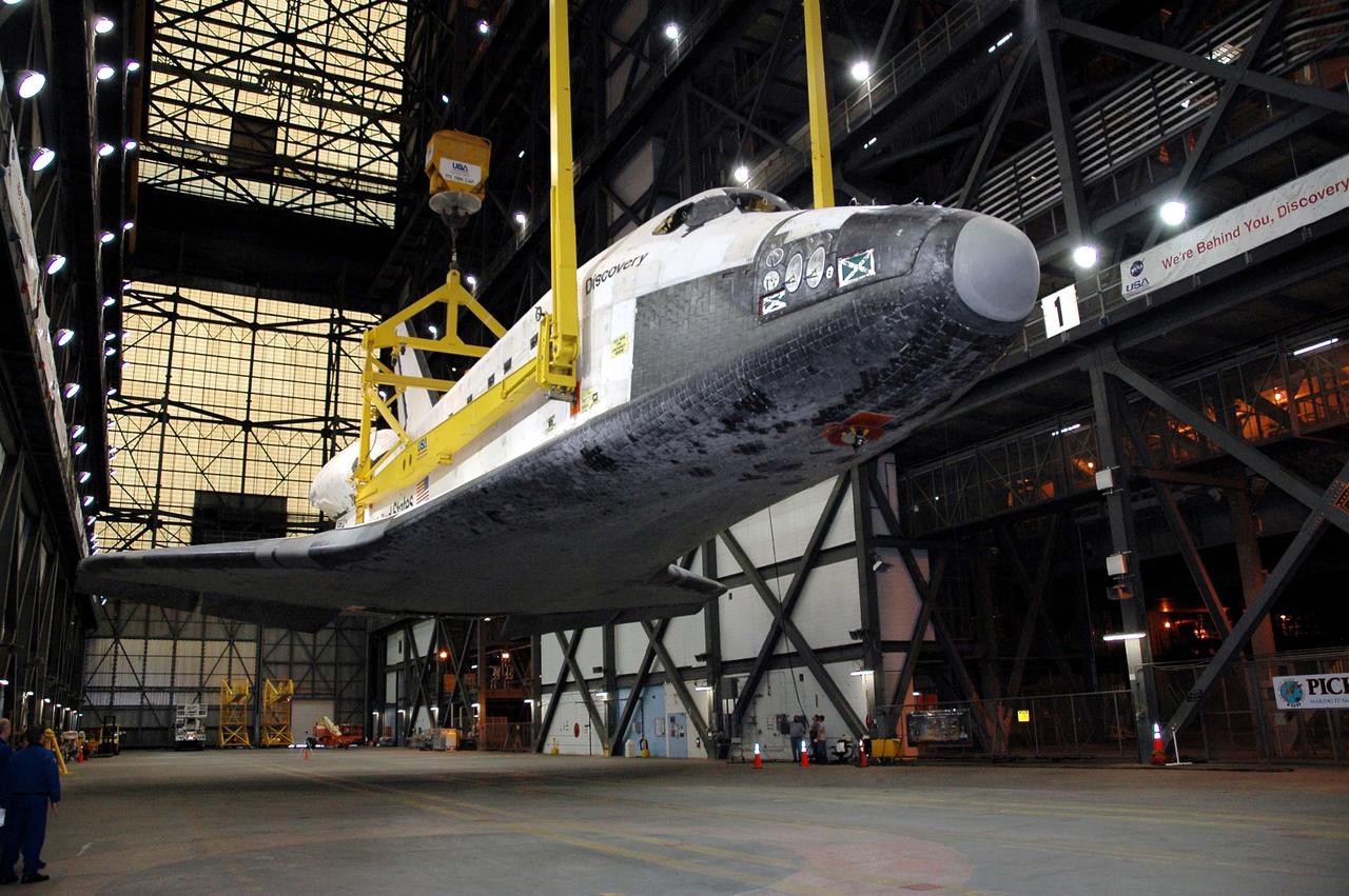 KENNEDY SPACE CENTER, FLA. - Suspended from an overhead crane, the orbiter Discovery is being raised to vertical in the transfer aisle of the Vehicle Assembly Building at NASA’s Kennedy Space Center. Discovery will be lifted up and lowered to the Solid Rocket Booster and External Tank already stacked on the top of the Mobile Launcher Platform (MLP). After Discovery has been mated to the External Tank_Solid Rocket Booster assembly on the MLP and all umbilicals have been connected, workers will perform an electrical and mechanical verification of the mated interfaces to verify all critical vehicle connections. A Shuttle interface test is performed using the launch processing system to verify Space Shuttle vehicle interfaces and Space Shuttle vehicle-to-ground interfaces. In approximately one week, Space Shuttle Discovery will be ready for rollout to Launch Pad 39B for Return to Flight mission STS-114. The launch window for STS-114 is May 15 to June 3.