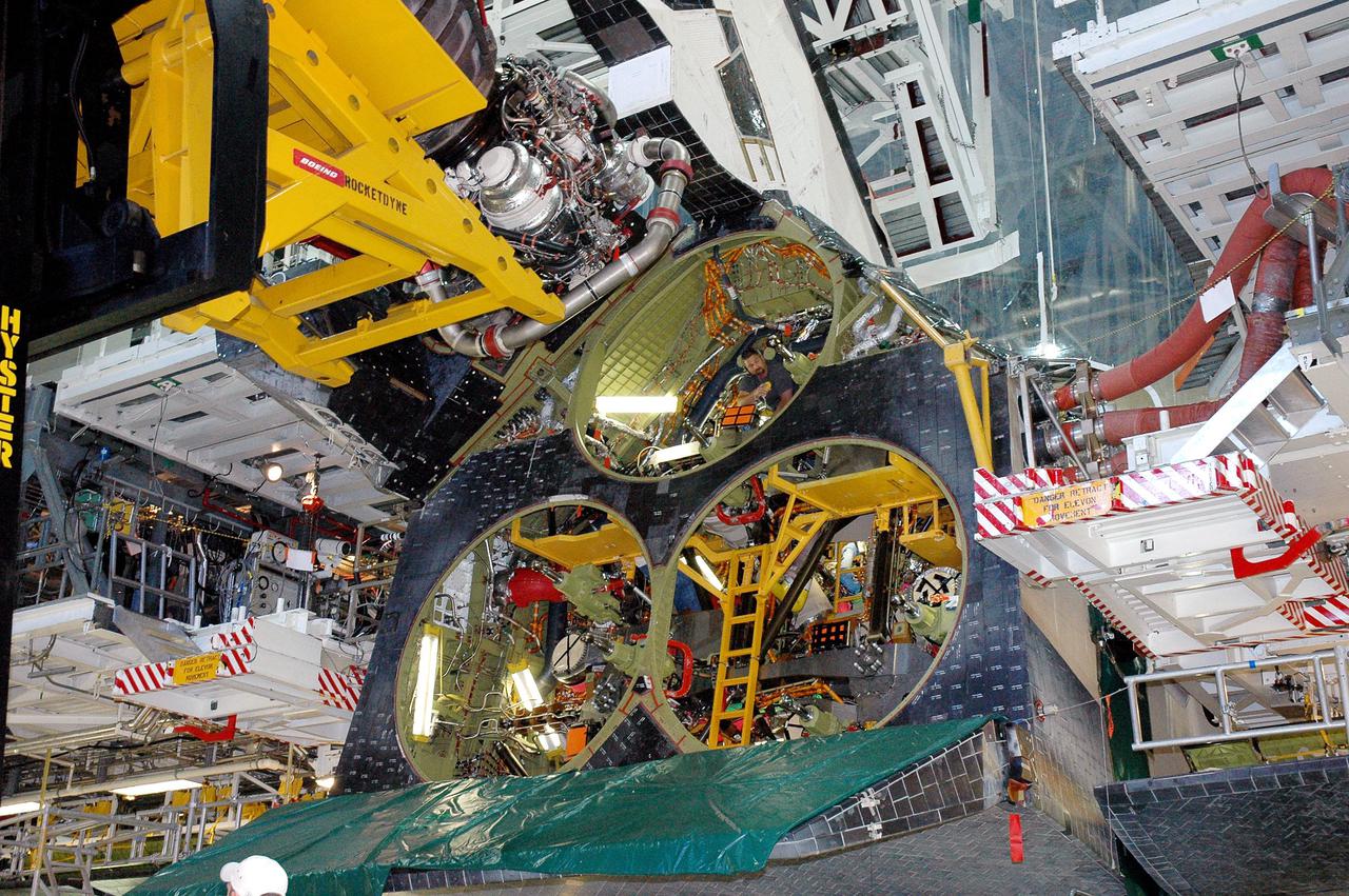 KENNEDY SPACE CENTER, FLA. -  In the Orbiter Processing Facility bay 1 at NASA’s Kennedy Space Center, a worker looks out from the position number one engine opening in Atlantis as a Hyster fork lift (left) holding a Space Shuttle Main Engine (SSME)  maneuvers into position for installation.  Overall, an SSME weighs approximately 7,000 pounds. Three engines provide the thrust, along with the two Solid Rocket Boosters, for liftoff.  After about 2 minutes, the two boosters are spent and are separated from the external tank. The SSMEs continue firing for about 8 minutes. They shut down just before the craft is inserted into orbit.  The SSMEs are tested at Stennis Space Center in Mississippi.  Atlantis is being processed for the second Return to Flight mission, STS-121, scheduled for launch in a window from July 12 through July 31.
