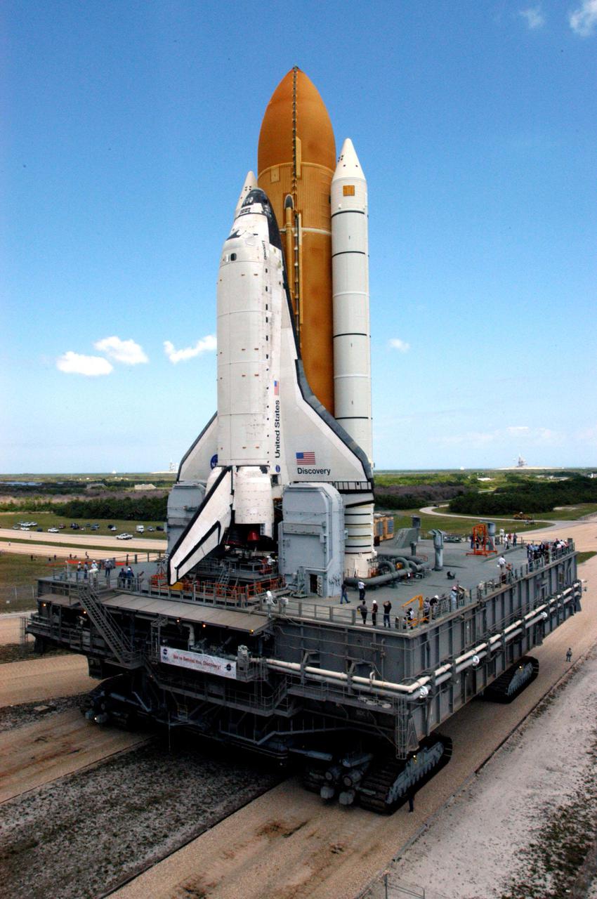 KENNEDY SPACE CENTER, FLA. -  Under brilliant-blue Florida skies, Space Shuttle Discovery, atop the Mobile Launcher Platform, is on its way to Launch Pad 39B at NASA’s Kennedy Space Center.  First motion out of the Vehicle Assembly Building (VAB)  was at 2:04 p.m. EDT.  The Shuttle comprises the orbiter, External Tank (ET) and twin Solid Rocket Boosters (SRBs).  The  Mobile Launcher Platform moved by the Crawler-Transporter underneath.  The Crawler is 20 feet high, 131 feet long and 114 feet wide.  It moves on eight tracks, each containing 57 shoes, or cleats, weighing one ton each.  Loaded with the Space Shuttle, the Crawler can move at a maximum speed of approximately 1 mile an hour. A leveling system in the Crawler keeps the Shuttle vertical while negotiating the 5 percent grade leading to the top of the launch pad.  Launch of Discovery on its Return to Flight mission, STS-114, is targeted for May 15 with a launch window that extends to June 3. During its 12-day mission, Discovery’s seven-person crew will test new hardware and techniques to improve Shuttle safety, as well as deliver supplies to the International Space Station.  Discovery was moved on March 29 from the Orbiter Processing Facility to the VAB and attached to its propulsion elements, a redesigned ET and twin SRBs.