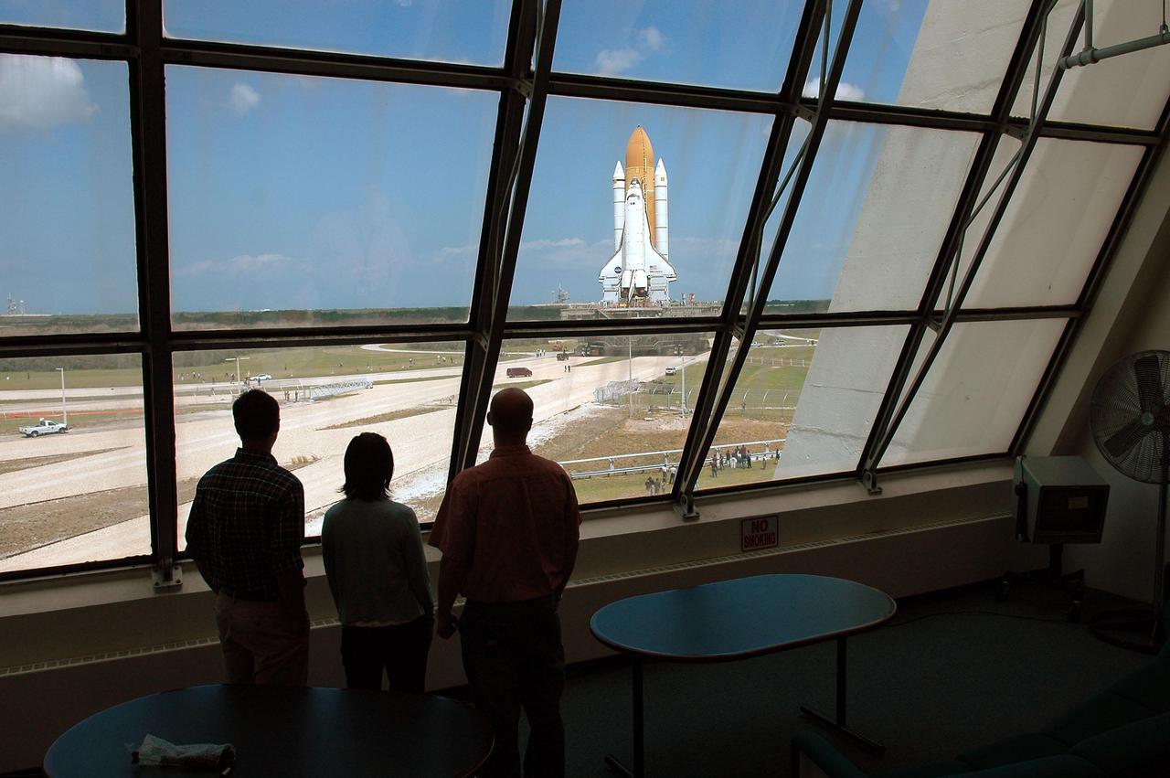 KENNEDY SPACE CENTER, FLA. -  From inside the viewing room of the Launch Control Center, KSC employees watch Space Shuttle Discovery as it creeps along the crawlerway toward the horizon, and Launch Pad 39B at NASA’s Kennedy Space Center.  First motion of the Shuttle out of the Vehicle Assembly Building (VAB)  was at 2:04 p.m. EDT. The Mobile Launcher Platform is moved by the Crawler-Transporter underneath.  The Crawler is 20 feet high, 131 feet long and 114 feet wide.  It moves on eight tracks, each containing 57 shoes, or cleats, weighing one ton each.  Loaded with the Space Shuttle, the Crawler can move at a maximum speed of approximately 1 mile an hour. A leveling system in the Crawler keeps the Shuttle vertical while negotiating the 5 percent grade leading to the top of the launch pad.  Launch of Discovery on its Return to Flight mission, STS-114, is targeted for May 15 with a launch window that extends to June 3. During its 12-day mission, Discovery’s seven-person crew will test new hardware and techniques to improve Shuttle safety, as well as deliver supplies to the International Space Station.  Discovery was moved on March 29 from the Orbiter Processing Facility to the VAB and attached to its propulsion elements, a redesigned ET and twin SRBs.
