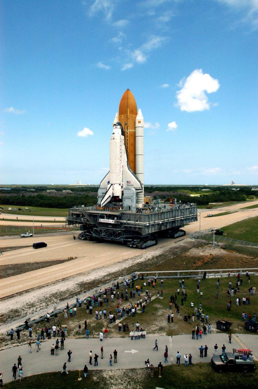 KENNEDY SPACE CENTER, FLA. -  As Space Shuttle Discovery creeps along the crawlerway toward the horizon, and Launch Pad 39B at NASA’s Kennedy Space Center, media and workers in the foreground appear as ants.  First motion of the Shuttle out of the Vehicle Assembly Building (VAB)  was at 2:04 p.m. EDT. The Mobile Launcher Platform is moved by the Crawler-Transporter underneath.  The Crawler is 20 feet high, 131 feet long and 114 feet wide.  It moves on eight tracks, each containing 57 shoes, or cleats, weighing one ton each.  Loaded with the Space Shuttle, the Crawler can move at a maximum speed of approximately 1 mile an hour. A leveling system in the Crawler keeps the Shuttle vertical while negotiating the 5 percent grade leading to the top of the launch pad.  Launch of Discovery on its Return to Flight mission, STS-114, is targeted for May 15 with a launch window that extends to June 3. During its 12-day mission, Discovery’s seven-person crew will test new hardware and techniques to improve Shuttle safety, as well as deliver supplies to the International Space Station.  Discovery was moved on March 29 from the Orbiter Processing Facility to the VAB and attached to its propulsion elements, a redesigned ET and twin SRBs.