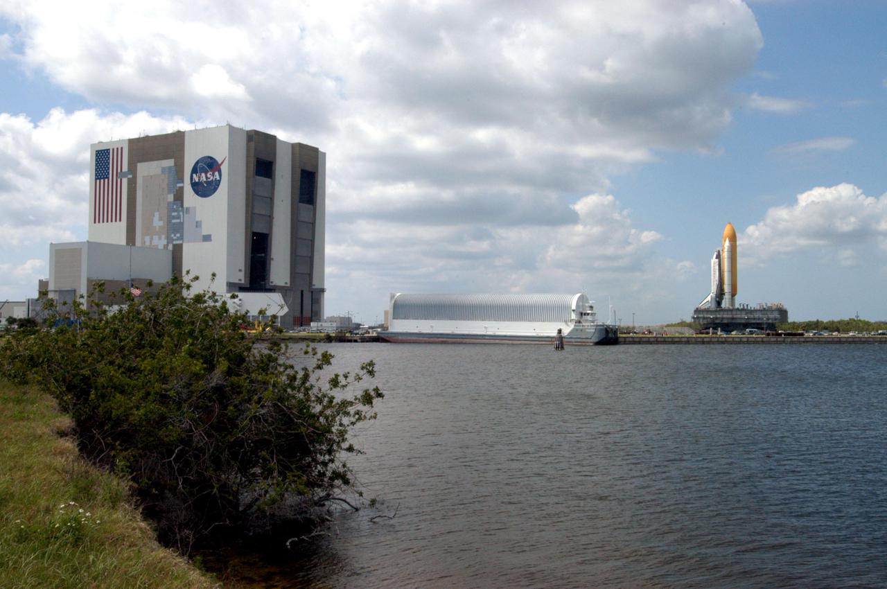 KENNEDY SPACE CENTER, FLA. -  Across the Turn Basin is seen the Vehicle Assembly Building (VAB (at left), the Launch Control Center (middle), and Space Shuttle Discovery (at right).    First motion of the Shuttle out of the VAB was at 2:04 p.m. EDT.  Atop the Mobile Launcher Platform, the Shuttle is on its way to Launch Pad 39B, marking a major milestone in Return to Flight.  The Mobile Launcher Platform is moved by the Crawler-Transporter underneath.  The Crawler is 20 feet high, 131 feet long and 114 feet wide.  It moves on eight tracks, each containing 57 shoes, or cleats, weighing one ton each.  Loaded with the Space Shuttle, the Crawler can move at a maximum speed of approximately 1 mile an hour. A leveling system in the Crawler keeps the Shuttle vertical while negotiating the 5 percent grade leading to the top of the launch pad.  Launch of Discovery on its Return to Flight mission, STS-114, is targeted for May 15 with a launch window that extends to June 3. During its 12-day mission, Discovery’s seven-person crew will test new hardware and techniques to improve Shuttle safety, as well as deliver supplies to the International Space Station.  Discovery was moved on March 29 from the Orbiter Processing Facility to the VAB and attached to its propulsion elements, a redesigned ET and twin SRBs.