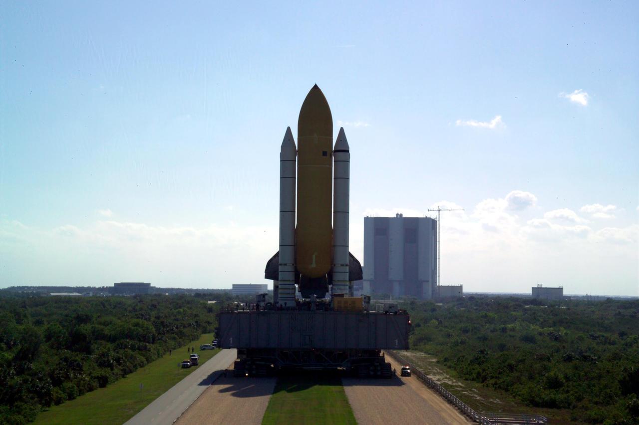 KENNEDY SPACE CENTER, FLA. -   At NASA’s Kennedy Space Center, Space Shuttle Discovery, atop the Mobile Launcher Platform (MLP), casts a shadow on the crawlerway as it makes its way east to Launch Complex 39B close to sunset.  In the background is the Vehicle Assembly Building (VAB) where Discovery began the rollout at 2:04 p.m. EDT. The rollout marks a major milestone in the Space Shuttle Program’s Return to Flight. The MLP is moved by the Crawler-Transporter underneath, which stands 20 feet high, 131 feet long and 114 feet wide.  It moves on eight tracks, each containing 57 shoes, or cleats, weighing one ton each.  Loaded with the Space Shuttle, the Crawler can move at a maximum speed of approximately 1 mile an hour. A leveling system in the Crawler keeps the Shuttle vertical while negotiating the 5 percent grade leading to the top of the launch pad.  Launch of Discovery on its Return to Flight mission, STS-114, is targeted for May 15 with a launch window that extends to June 3. During its 12-day mission, Discovery’s seven-person crew will test new hardware and techniques to improve Shuttle safety, as well as deliver supplies to the International Space Station.